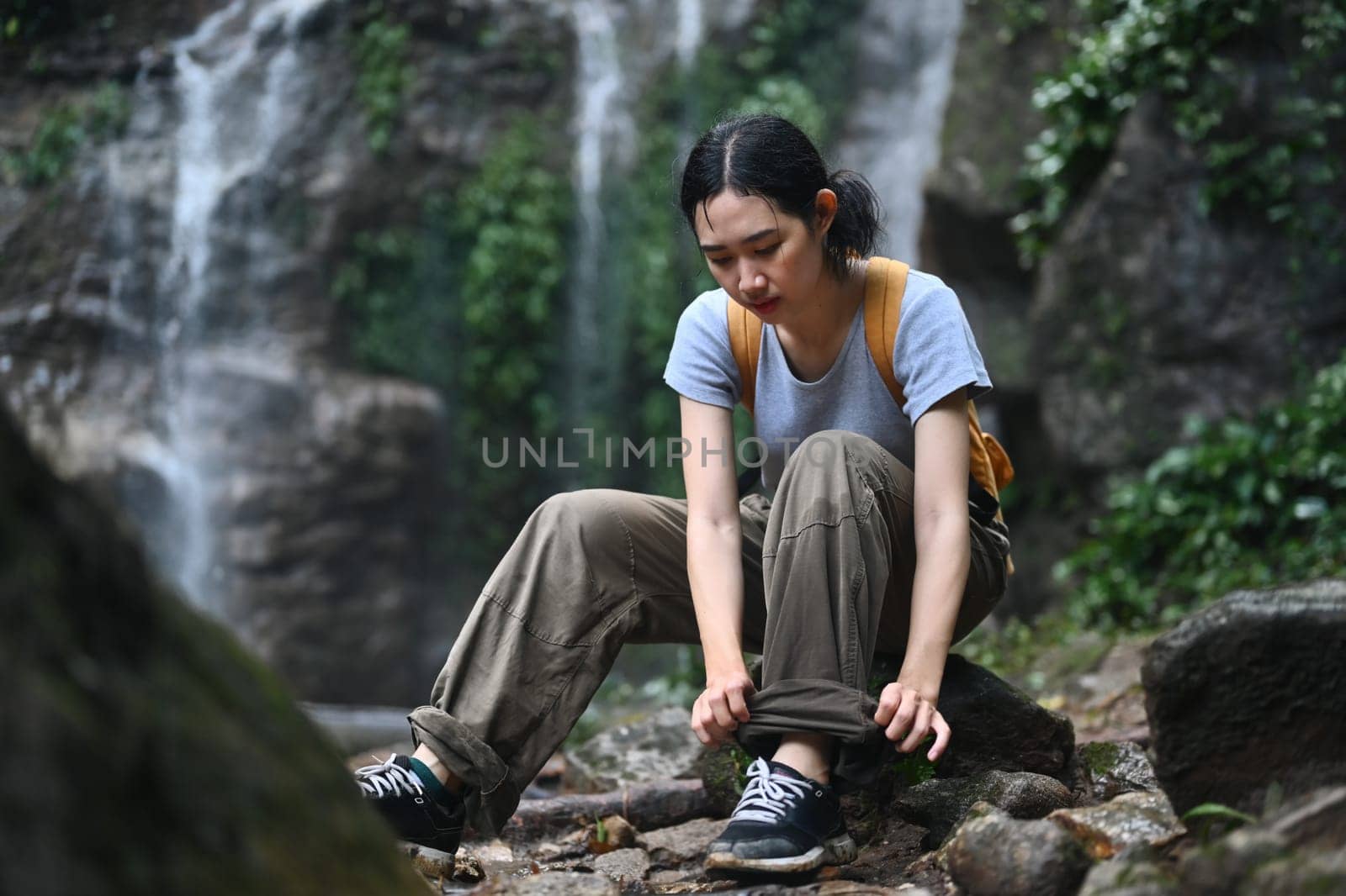 Young female hiker tying shoelaces and getting ready for trekking in forest. Active life concept.
