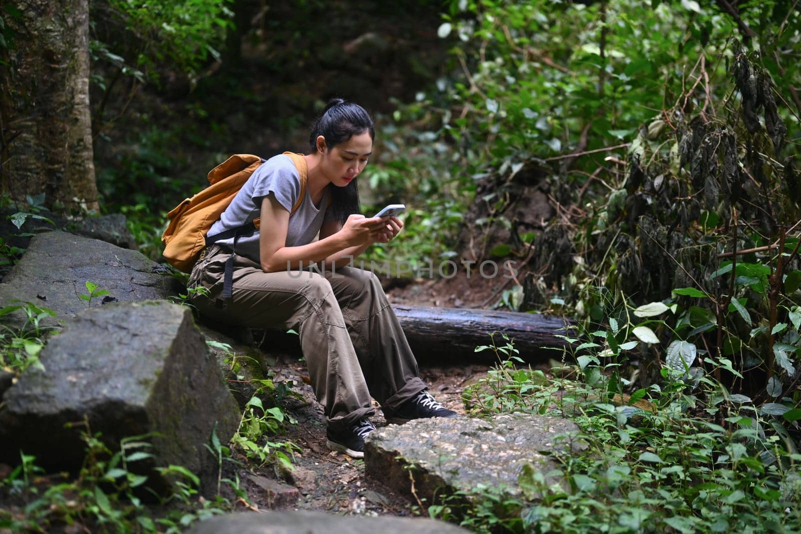 Tourist woman with backpack using mobile phone in forest. Travel, vacation and adventure concept.