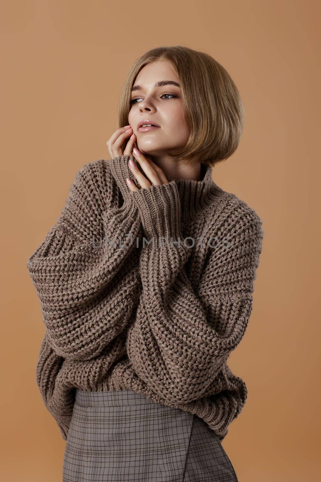 beautiful blonde woman in brown knitted sweater on beige background. autumn style