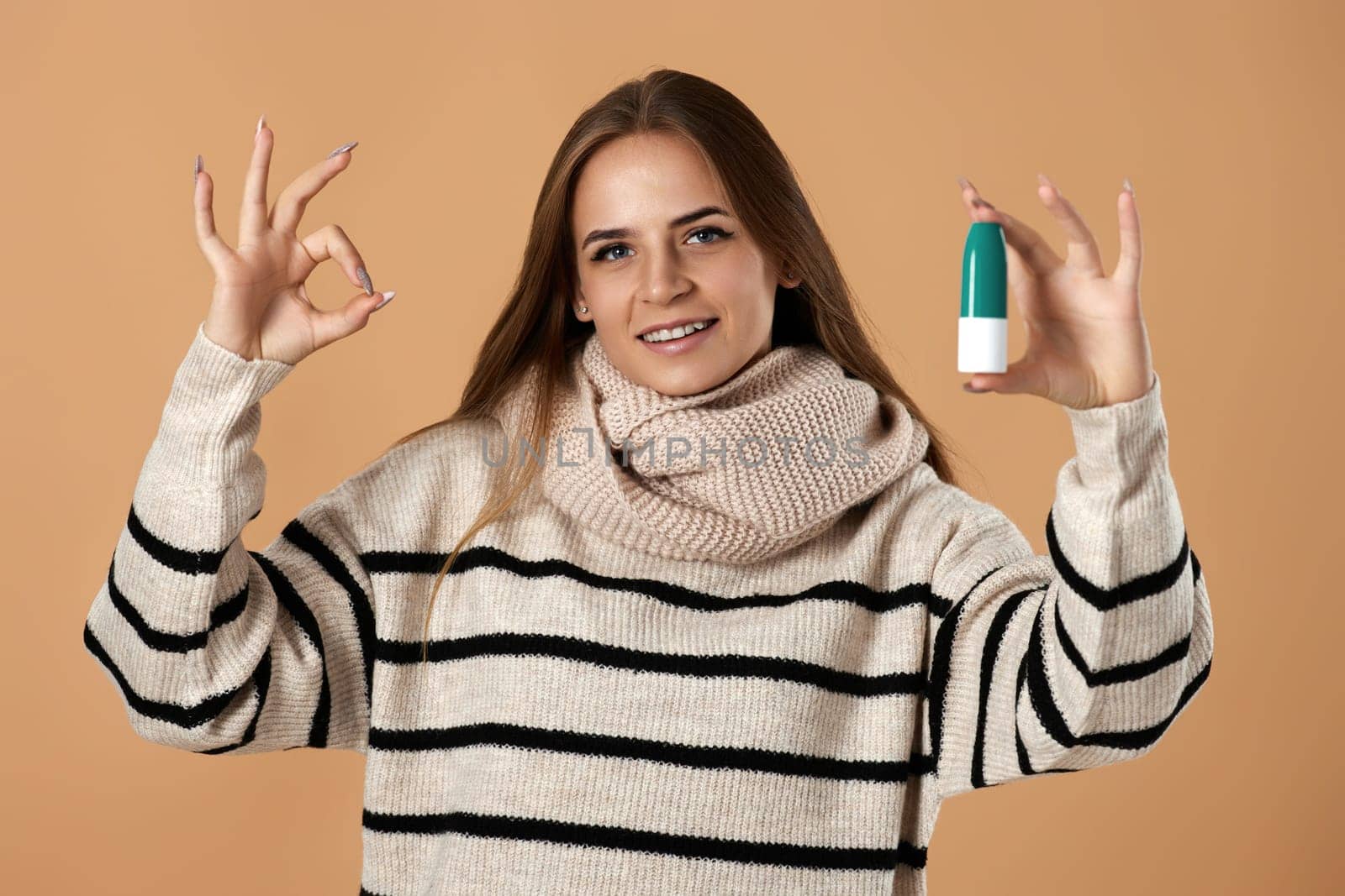 smiling caucasian woman holds nasal spray for allergies and showing Ok gesture on beige background.