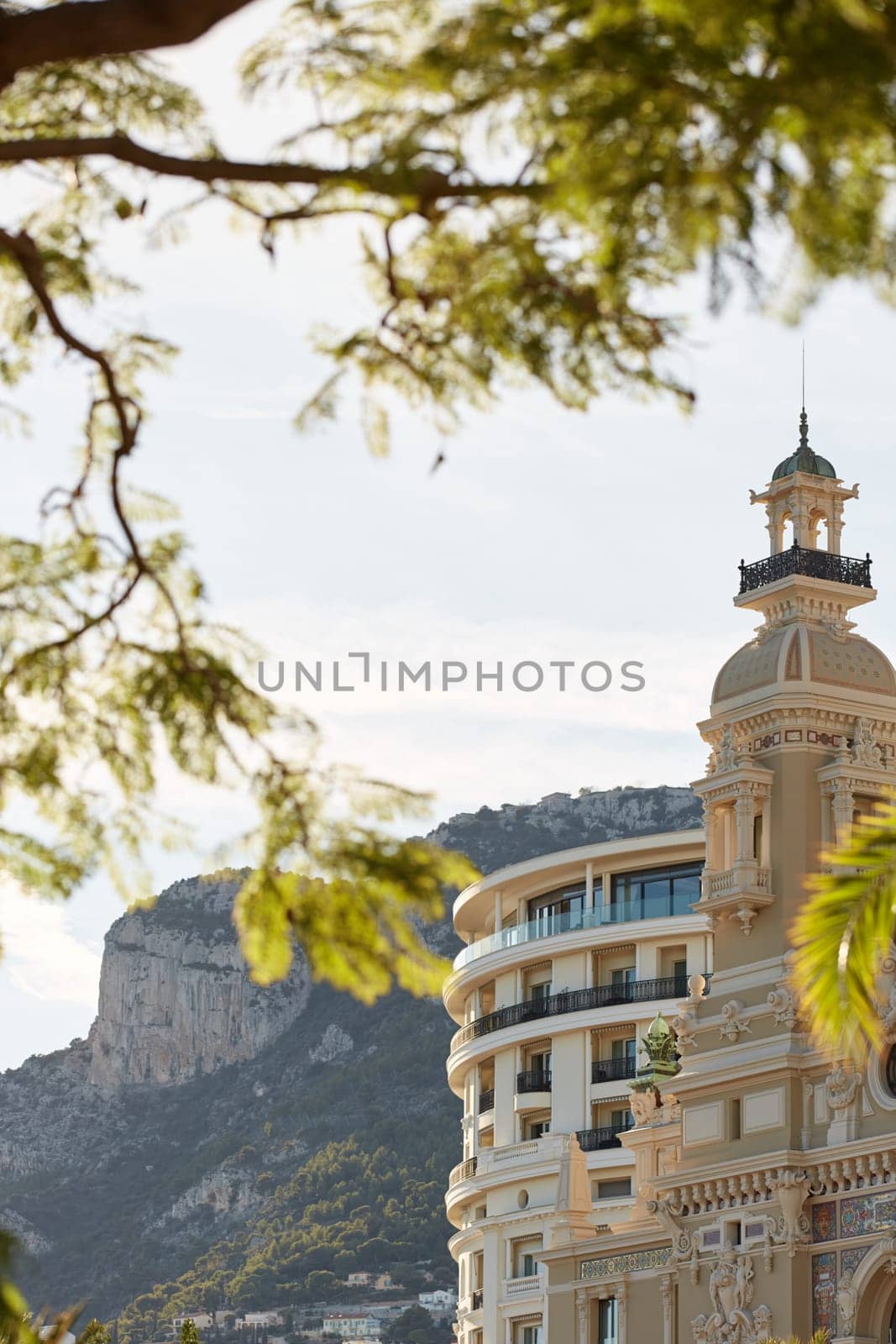 Monaco, Monte-Carlo, 21 October 2022: Towers of Casino Monte-Carlo at sunset, the famous hotel de Paris and mountain are on background, wealth life, famous landmark, pine trees, blue sky. High quality photo