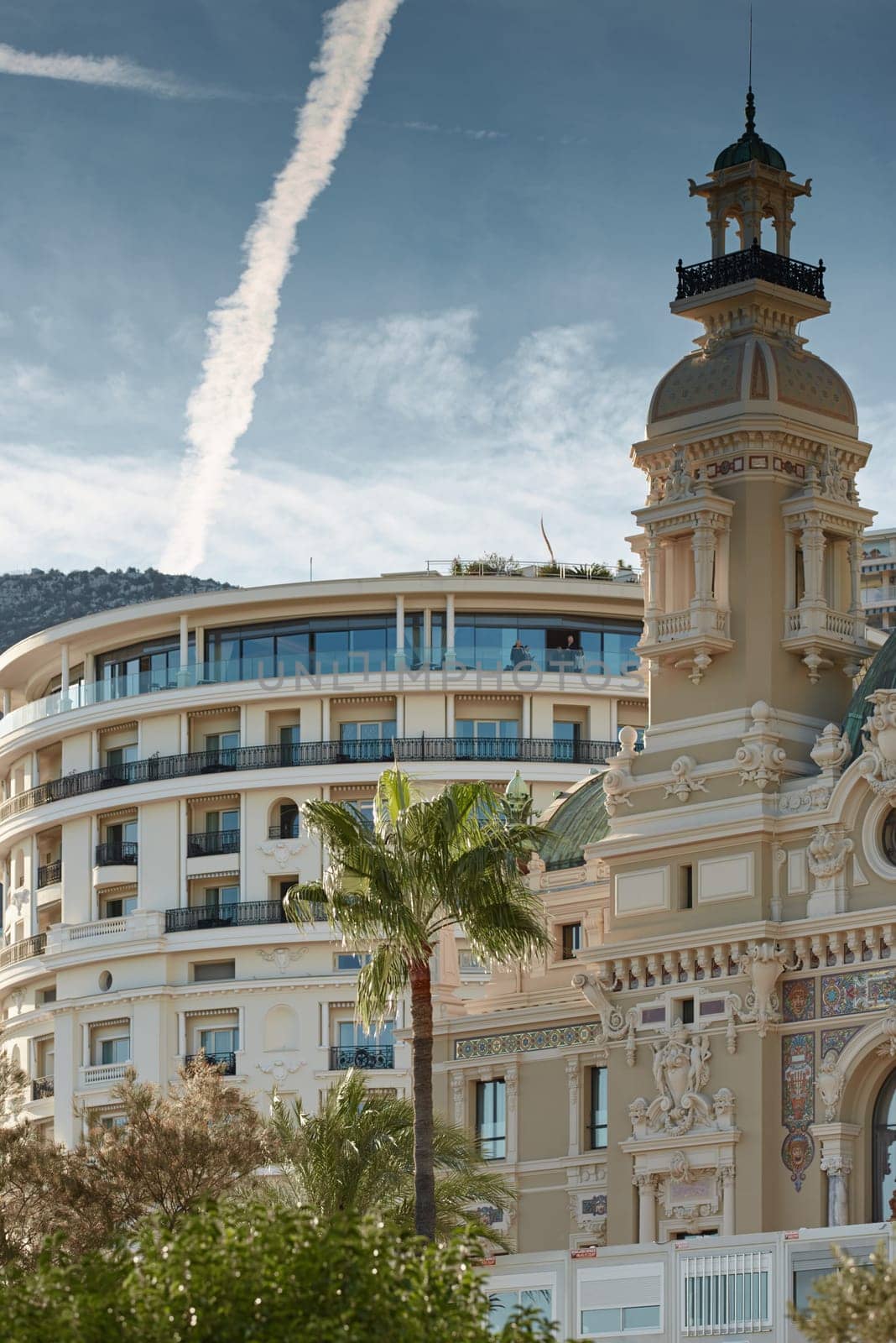 Monaco, Monte-Carlo, 21 October 2022: Towers of Casino Monte-Carlo at sunset, the famous hotel de Paris and mountain are on background, wealth life, famous landmark, pine trees, blue sky. High quality photo