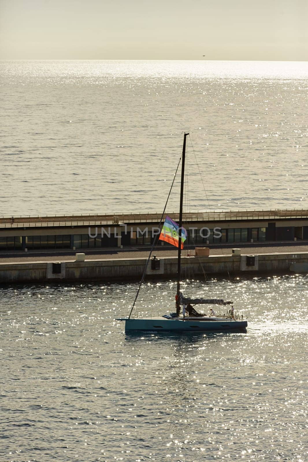 Monaco, Monte Carlo, 23 October 2022: sailing boat with lgbt flag leaves the port Hercules at sunset, the team prepares the boat, pier and mega yacht. High quality photo