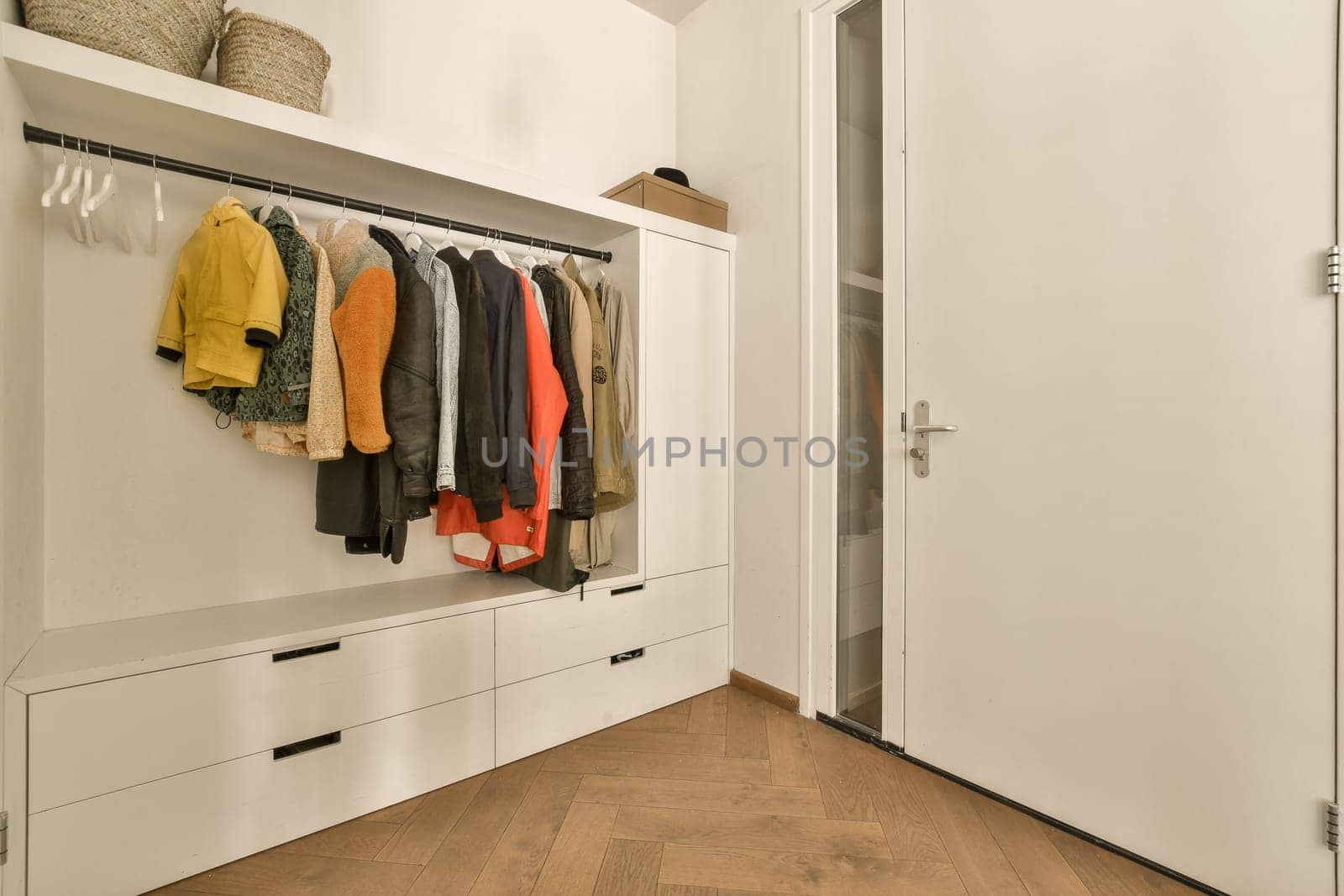 a closet with clothes hanging on the wall and wooden flooring in front of white cabinetd cupboards filled with colorful sweaters