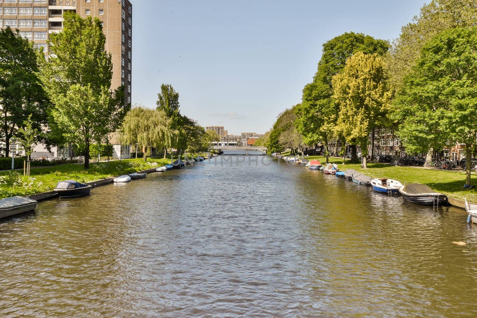 some boats in the water and buildings on the other side of the river, with trees lining the canal behind