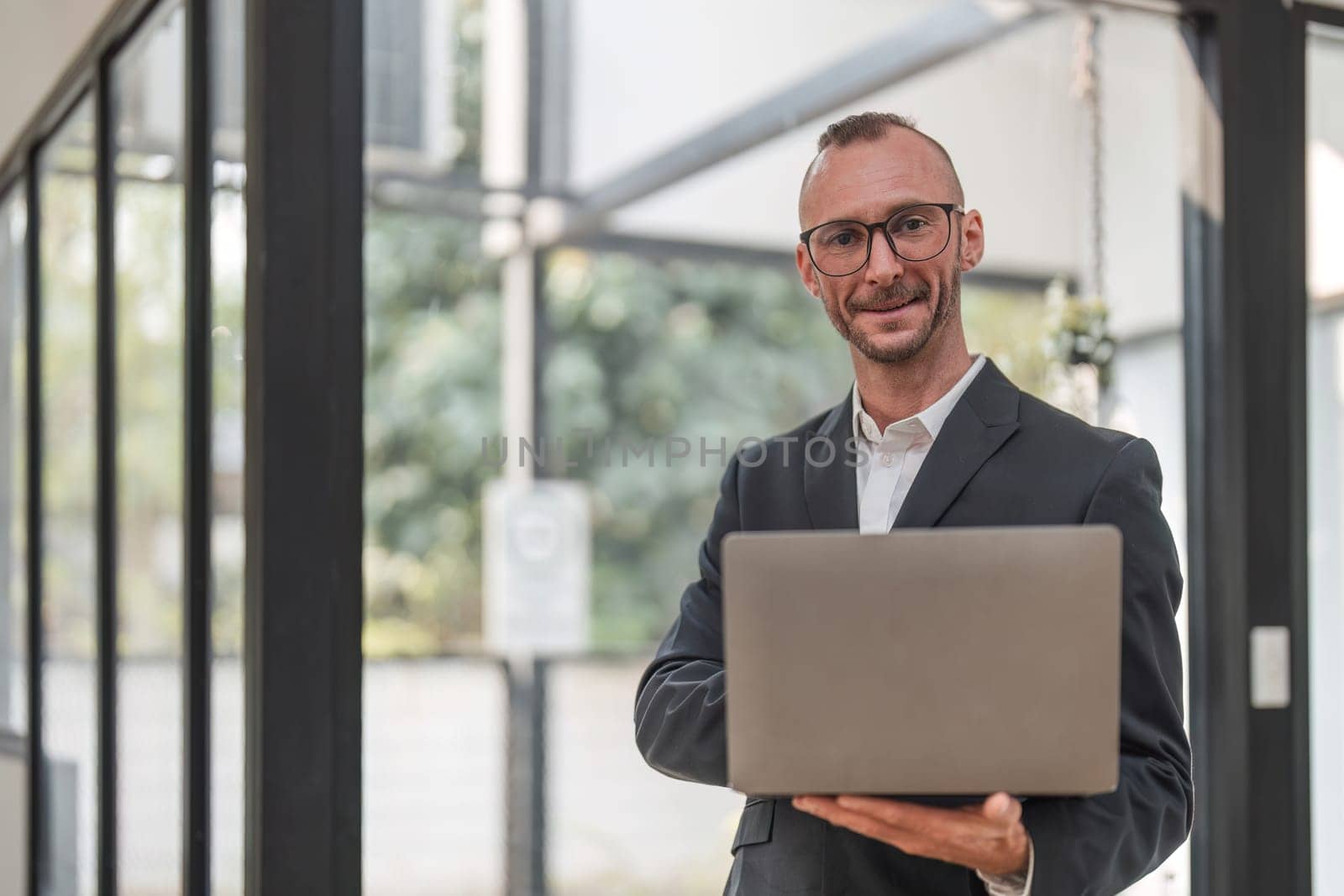 Successful businessman standing in modern office Use a laptop computer Organization or financial manager who is successful in planning investment projects by wichayada