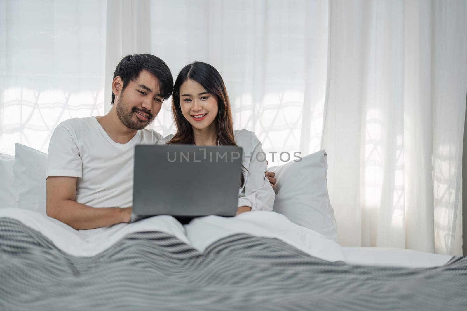 Photo of happy young couple using laptop while relaxing on bed at home. by wichayada