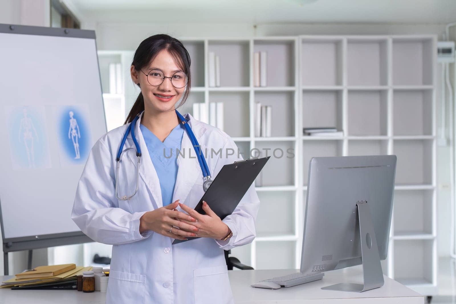 Portrait of a smiling female doctor holding a clipboard Wear a medical coat and stethoscope in a hospital office. Medical and healthcare concept by wichayada