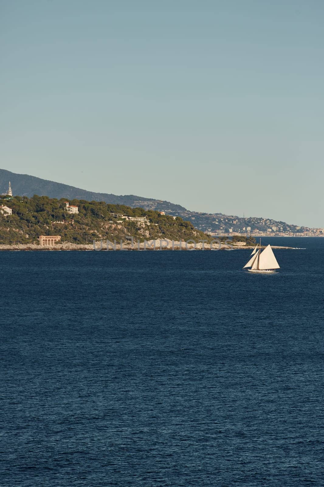 Monaco, huge sail yacht is in sea at sunset, island is nearby, wealth life of billionaires, mountains on background. High quality photo
