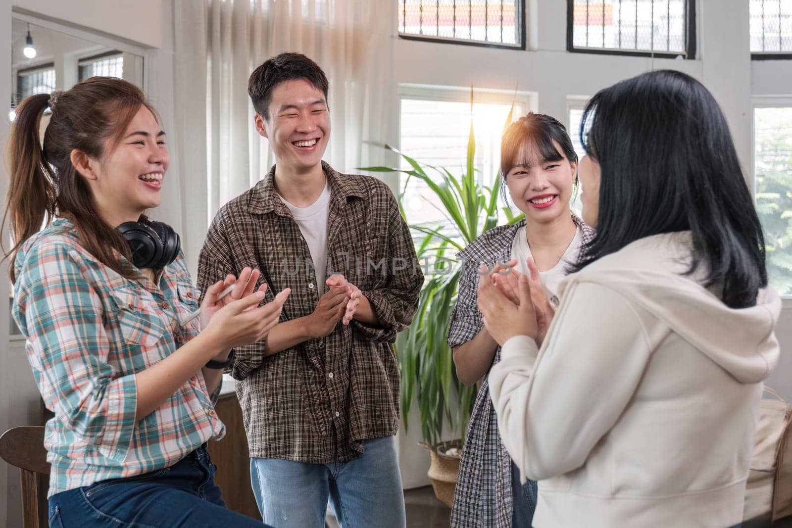 A group of cheerful and happy young Asian friends are gathering together to celebrate the success of a project together in a conference room. by wichayada