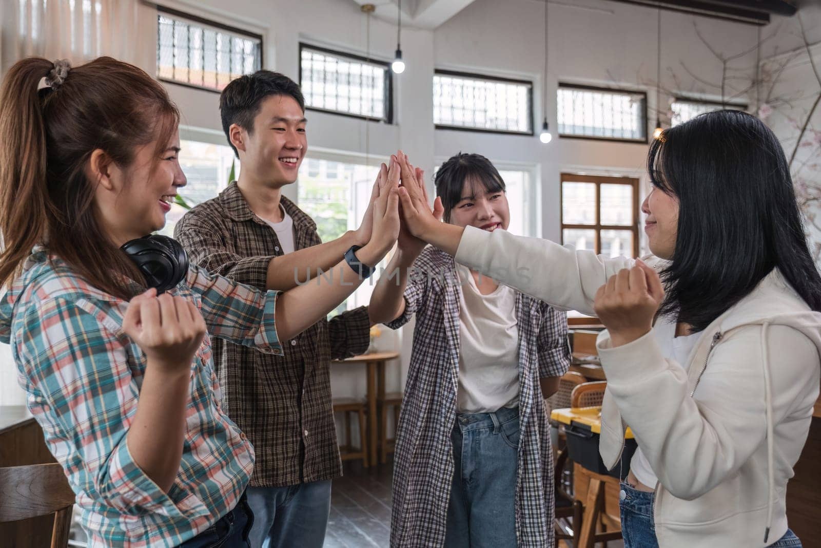 A group of cheerful and happy young Asian friends are gathering together to celebrate the success of a project together in a conference room. by wichayada