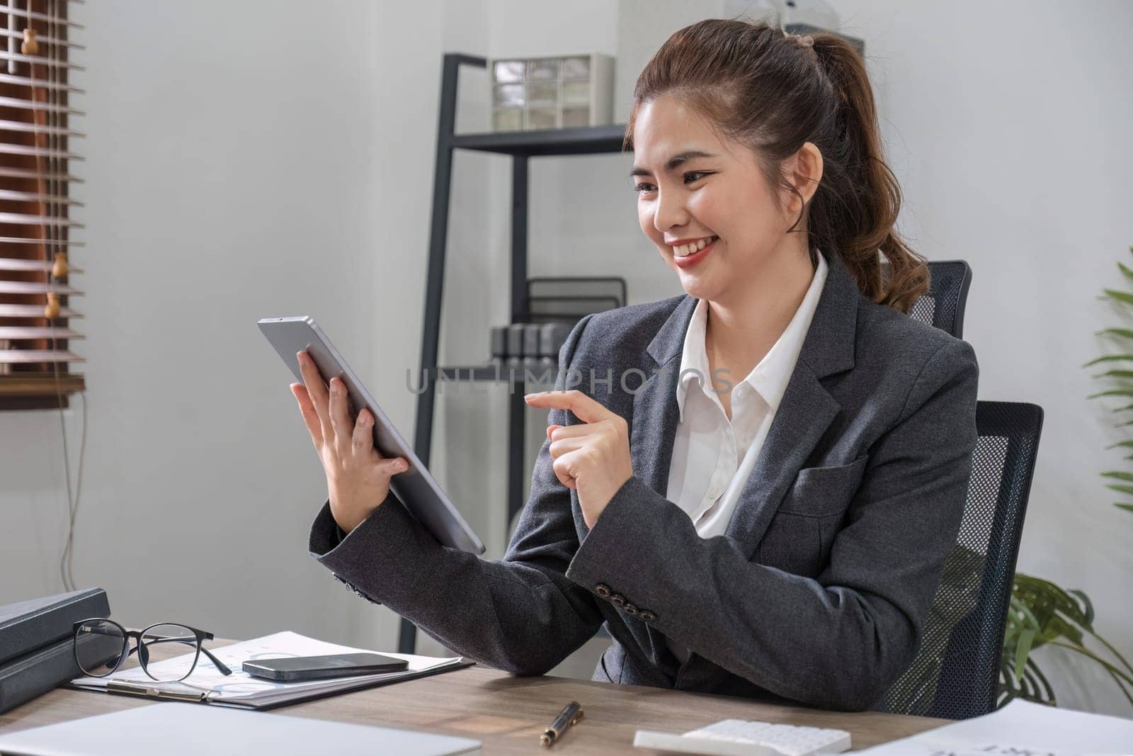 A young Asian office worker with a bright smile uses a tablet to plan work for his business team..