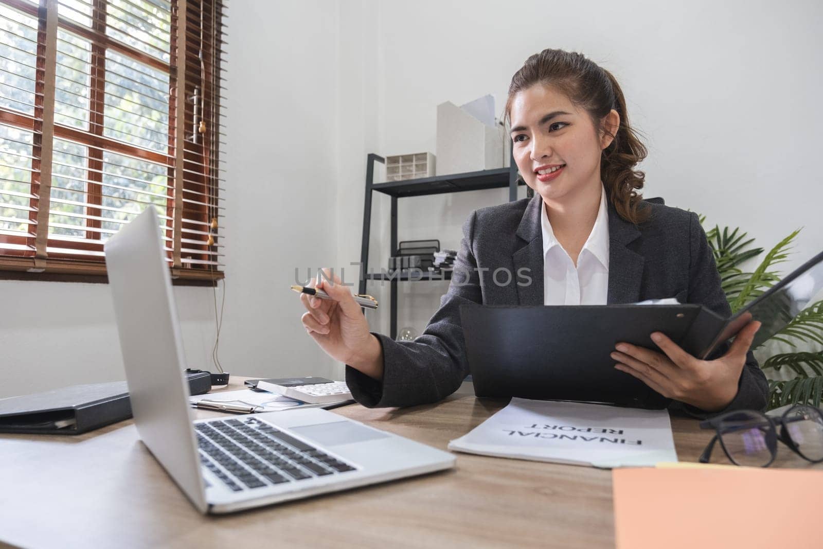 Young Asian office worker with a bright smile sits in front of her laptop computer. All work of the company is being reviewed..