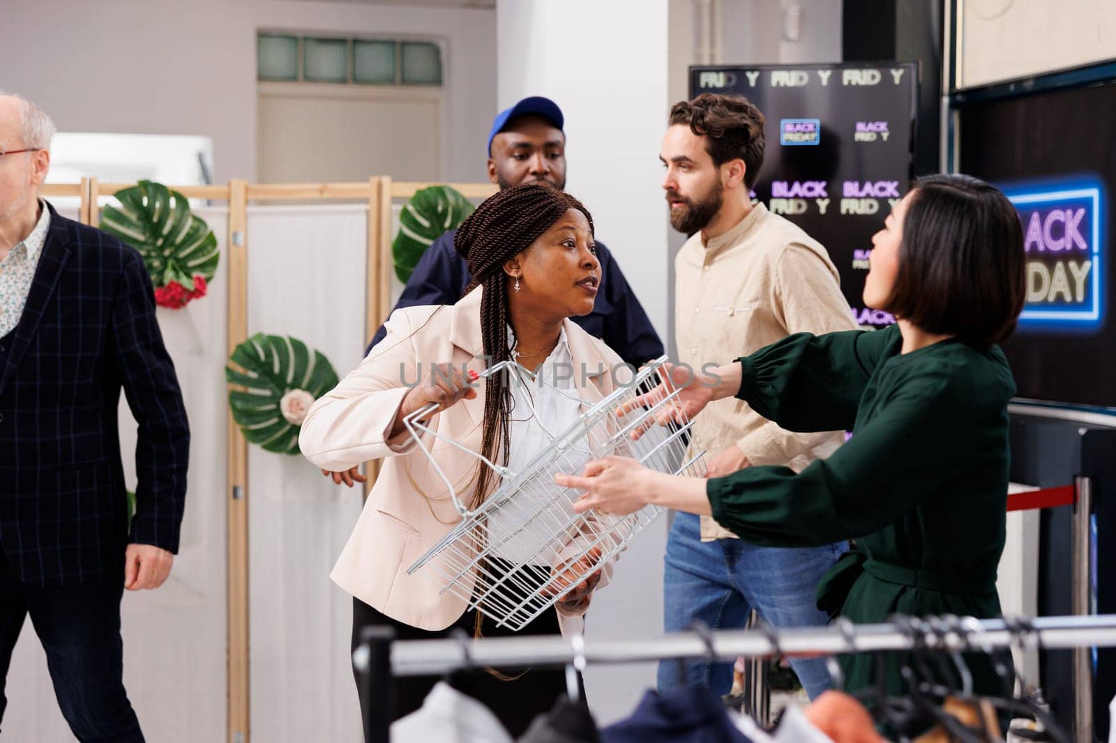 Mad angry diverse women customers arguing in clothing store, fighting for shopping basket during big sales in fashion boutique. Aggressive consumer behavior and Black Friday concept