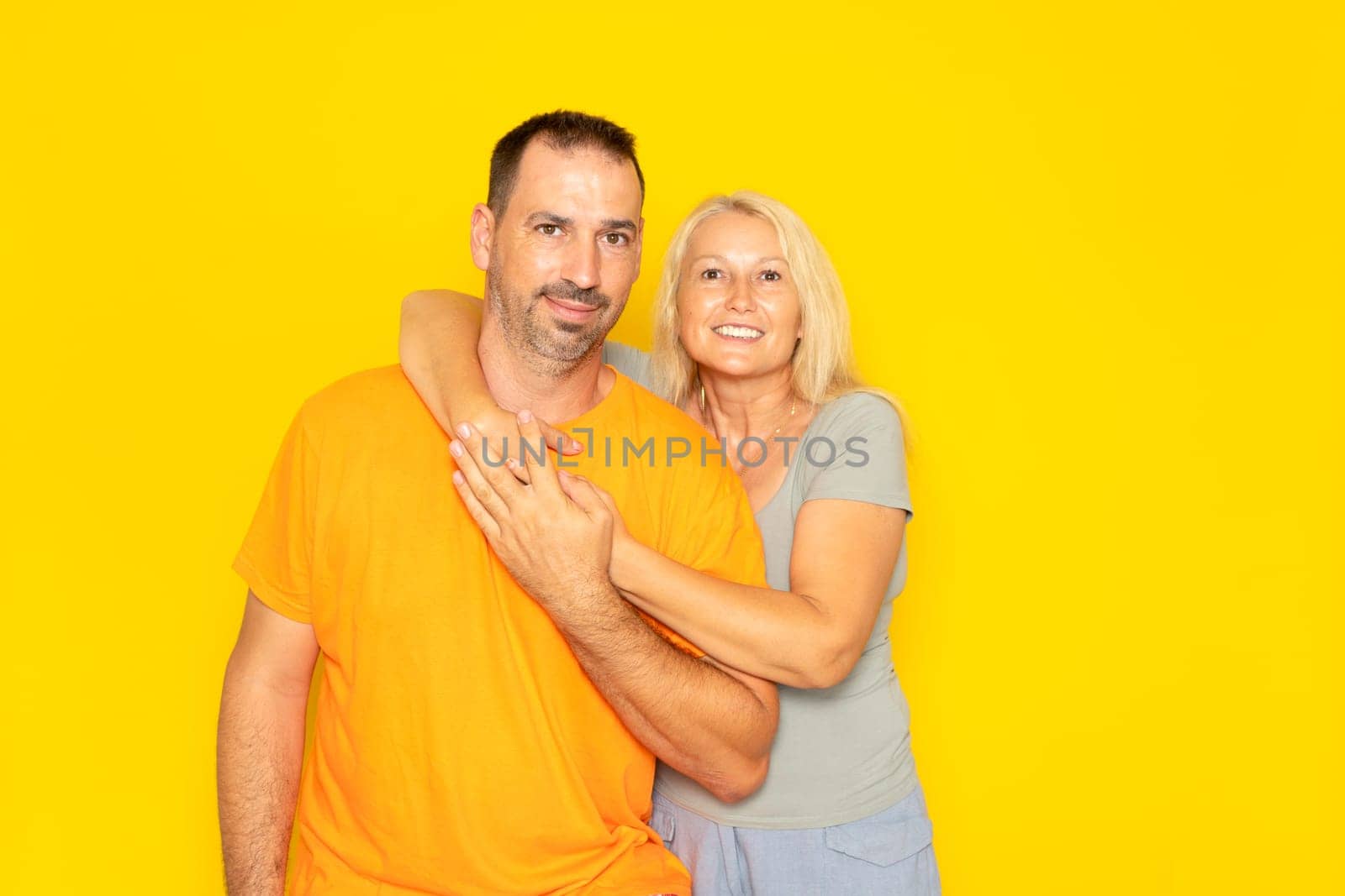 White happy couple hugging and looking at camera isolated over yellow background