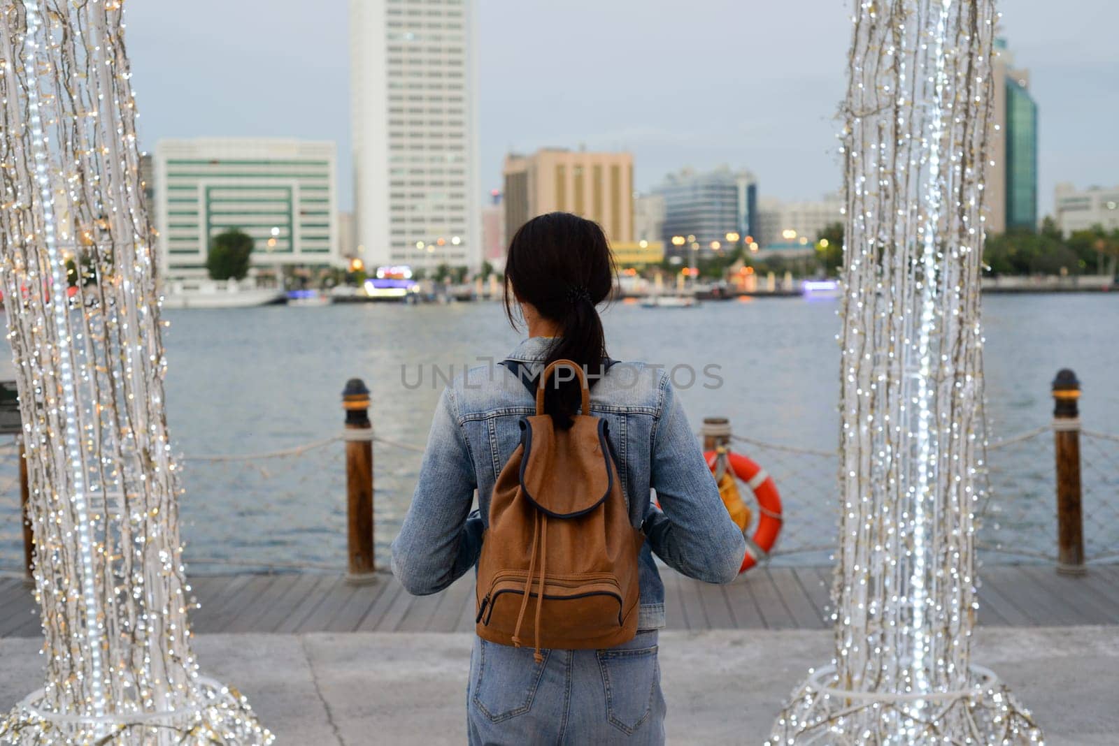 A young woman with a backpack on her back admires the architecture in the old Dubai Creek of Deira. Back view. Journey through the Persian Gulf. by Ekaterina34