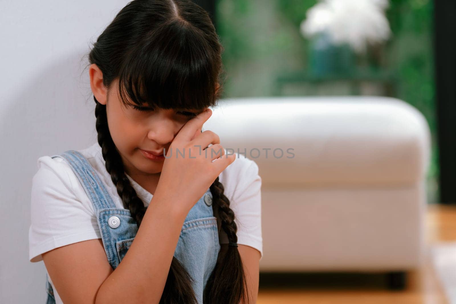 Sad little girl sitting alone in living room crying, feeling lonely. Young girl experiencing social isolation punishment or neglect from parent led to anxiety and traumatic in childhood. Synchronos