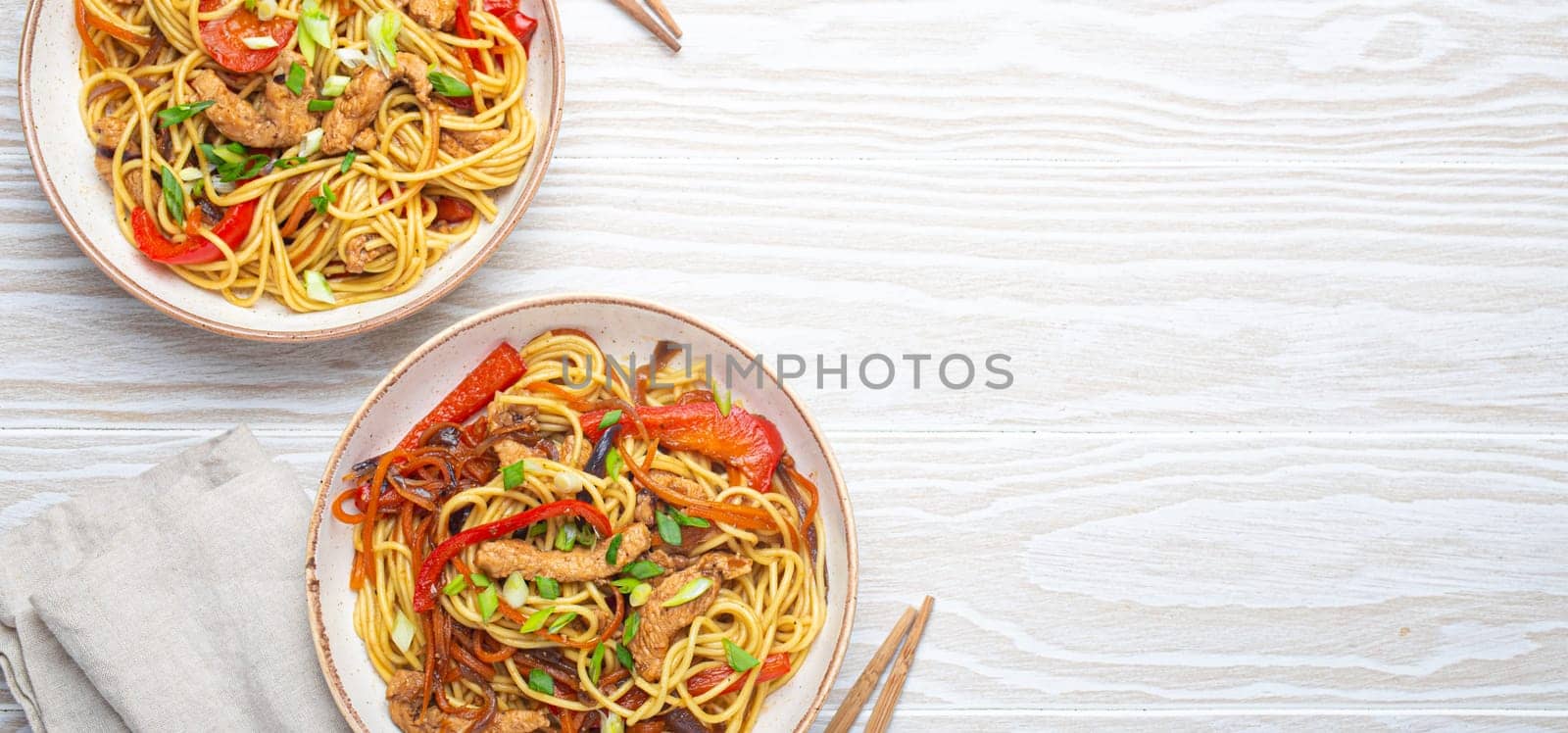 Two bowls with Chow Mein or Lo Mein, traditional Chinese stir fry noodles with meat and vegetables, served with chopsticks top view on rustic white wooden background table, space for text by its_al_dente