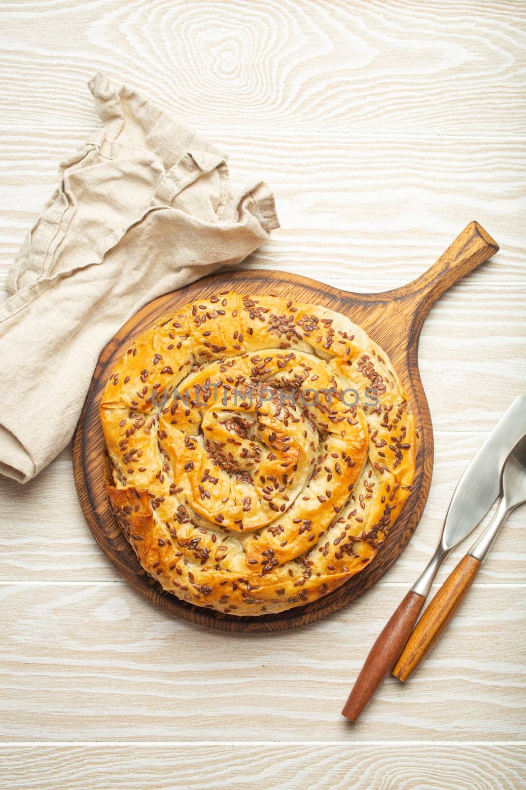 Burek made of filo dough with filling on cutting board, white wooden rustic background top view. Traditional savoury spiral pie of Balkans, Middle East and Central Asia.