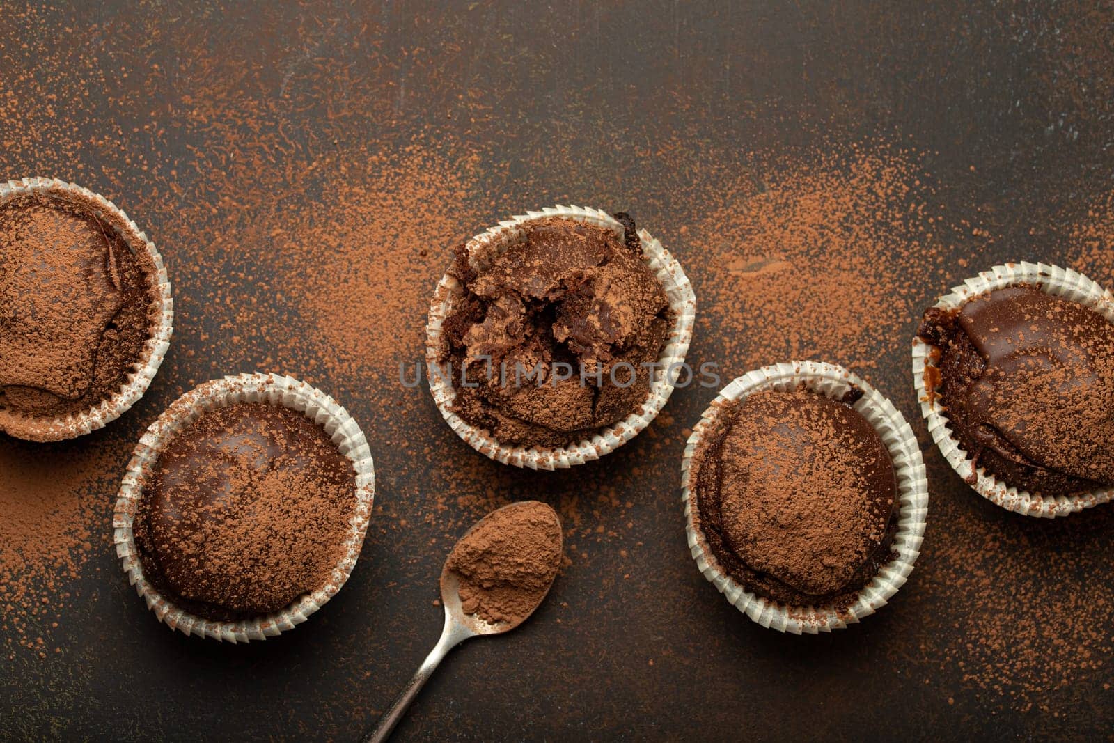 Chocolate browny muffins and cocoa in teaspoon top view on brown rustic stone background, sweet homemade dark chocolate cupcakes.