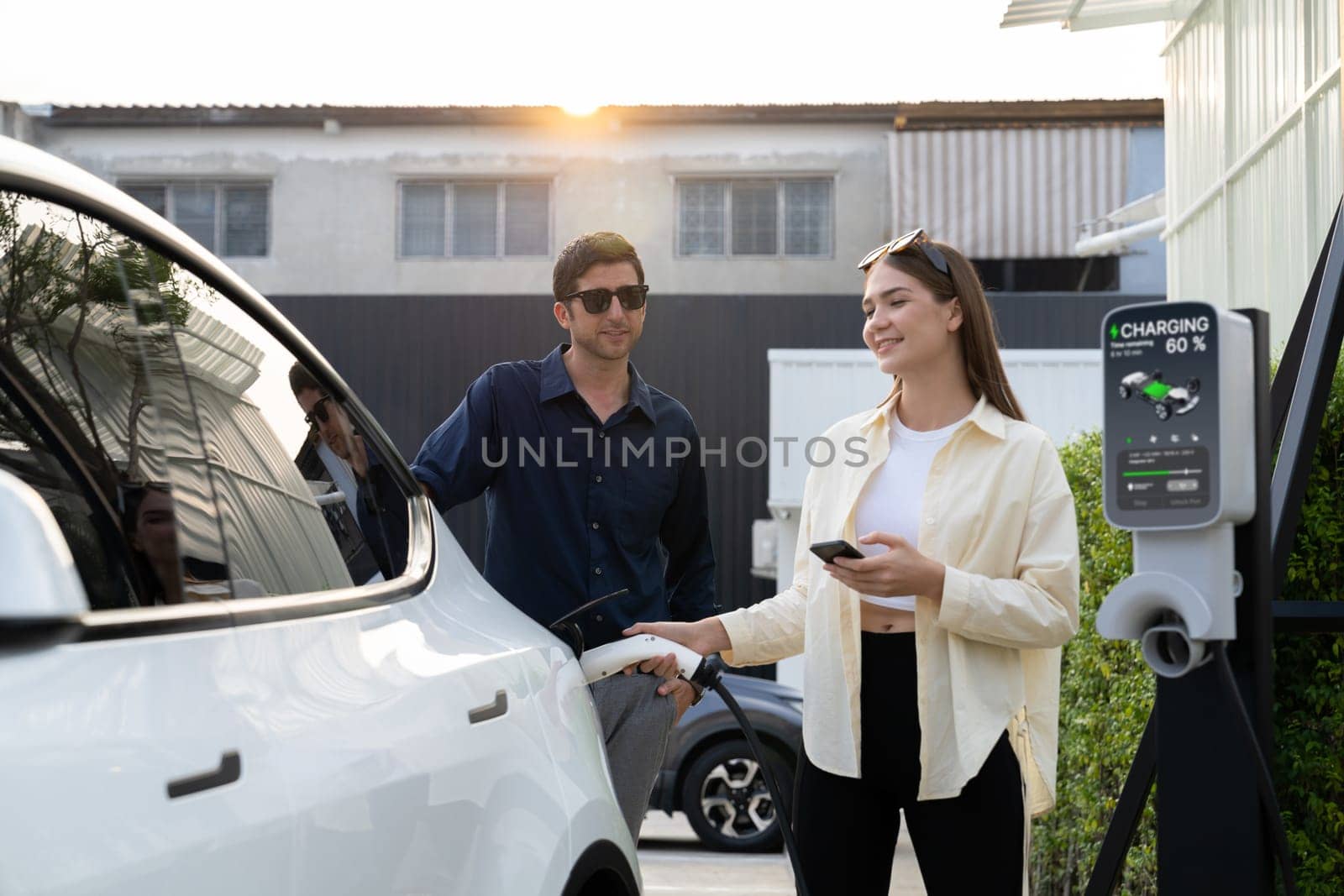 Eco-friendly conscious family couple recharging EV vehicle from home charging station. EV electric car technology utilized as alternative transportation for future sustainability. Expedient