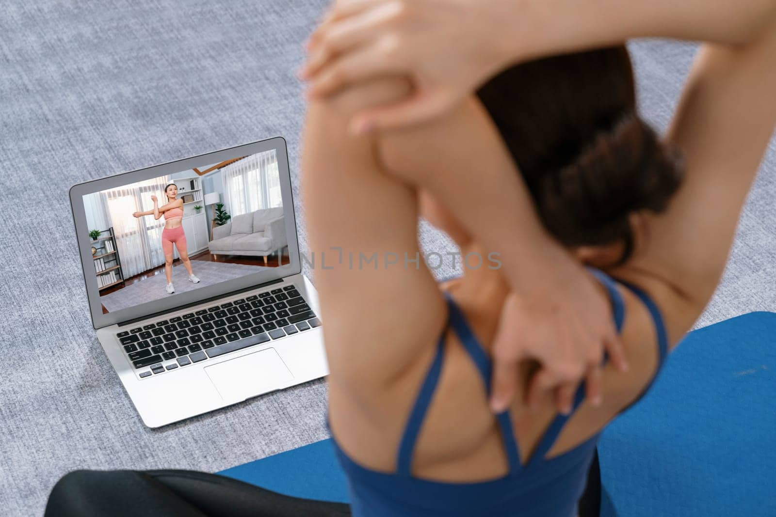 Asian woman in sportswear doing yoga exercise on fitness mat as her home workout training routine. Healthy body care lifestyle woman watching online yoga video on laptop. Vigorous