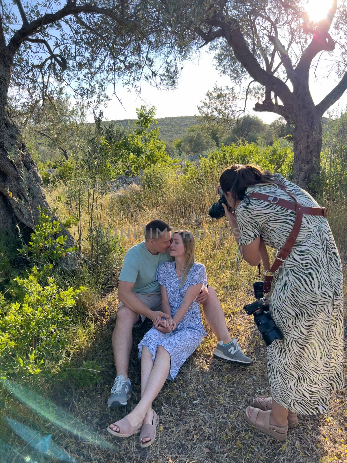 Photographer leaning over to take pictures of man and woman embracing, sitting on the grass. High quality photo