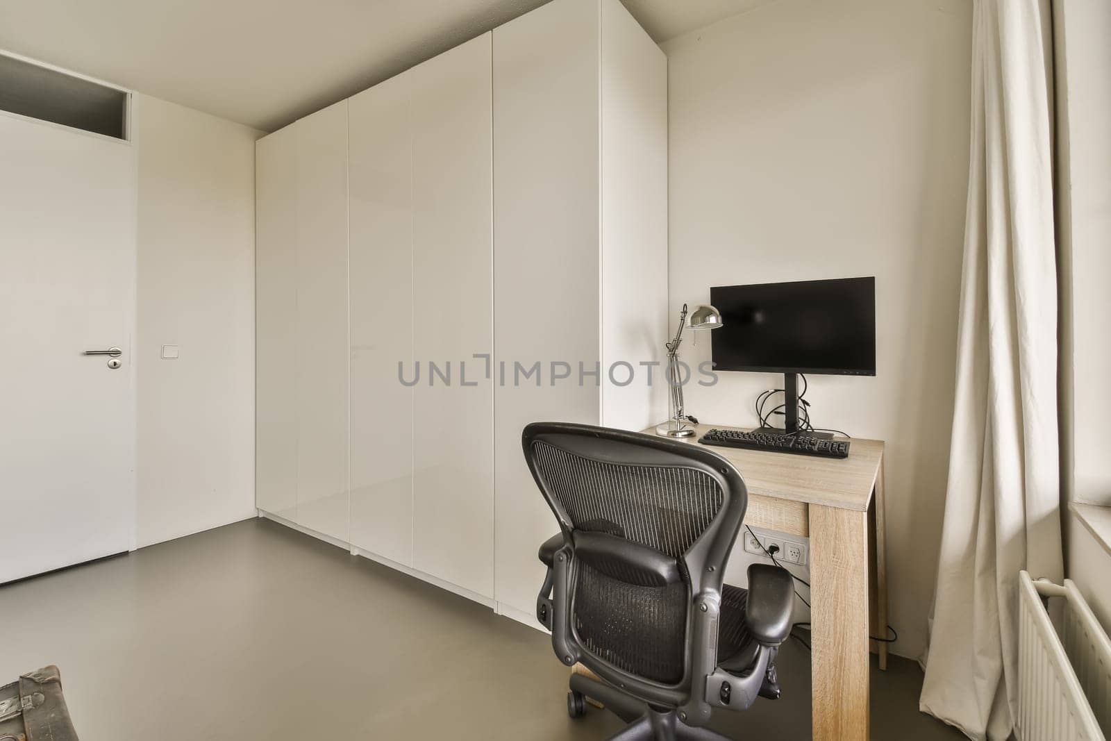 a room with an office chair, desk and television monitor on the wall in the room is very white color