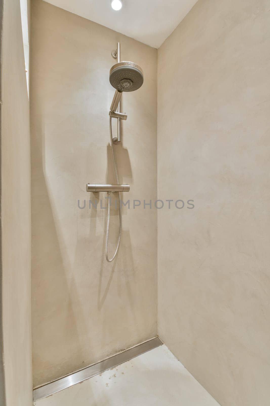 a shower in the corner of a room with beige walls and white tiles on the floor, there is a light coming from above