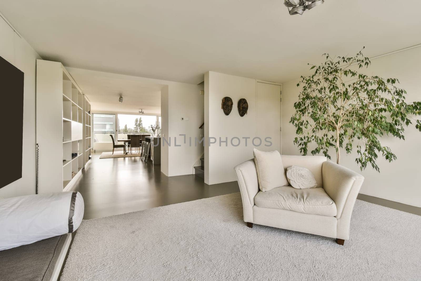 an empty living room with white carpet and large plant in the center of the room, there is a tv on the wall