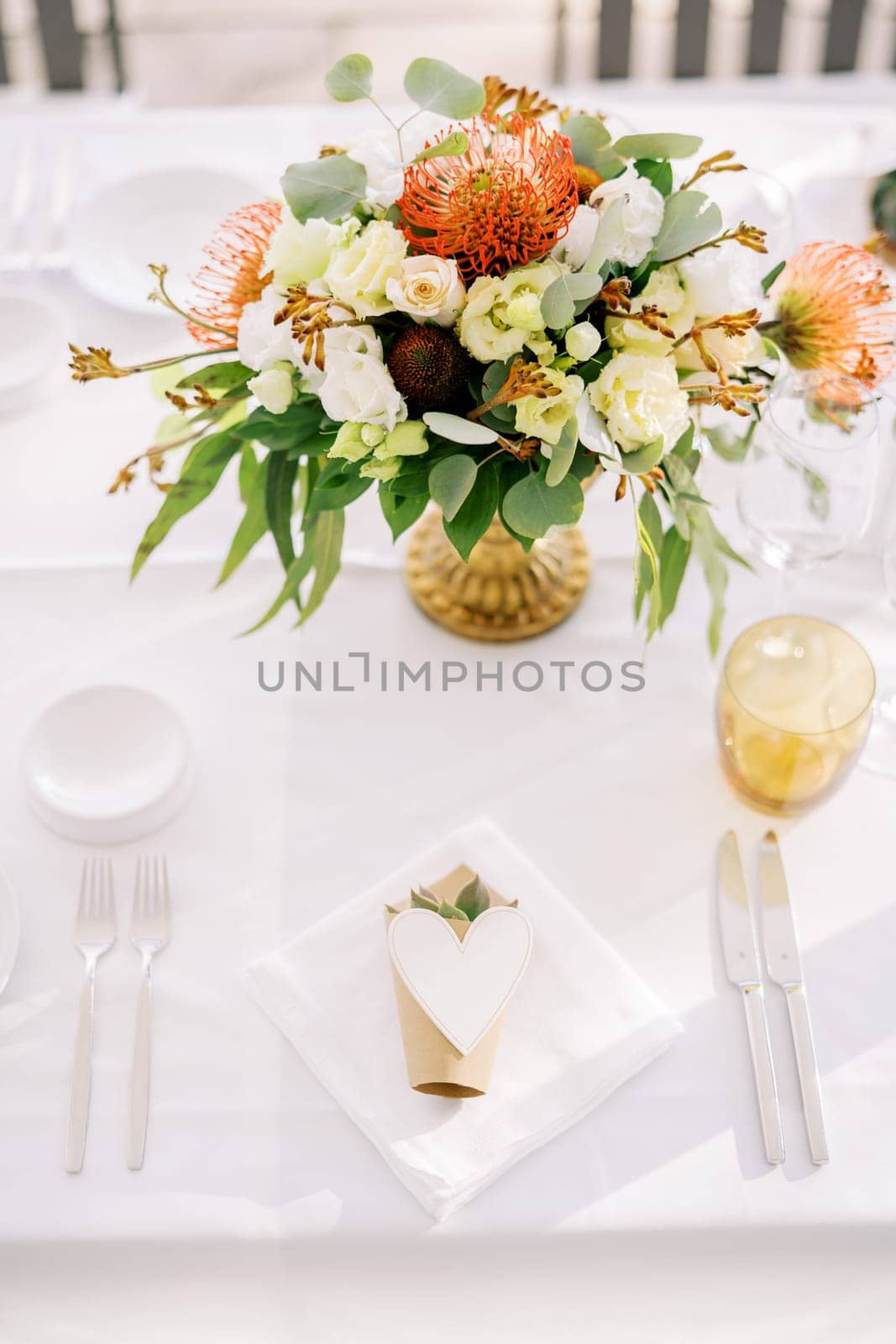 Bouquet of flowers stands on a festive table near an invitation with a paper heart on a napkin by Nadtochiy