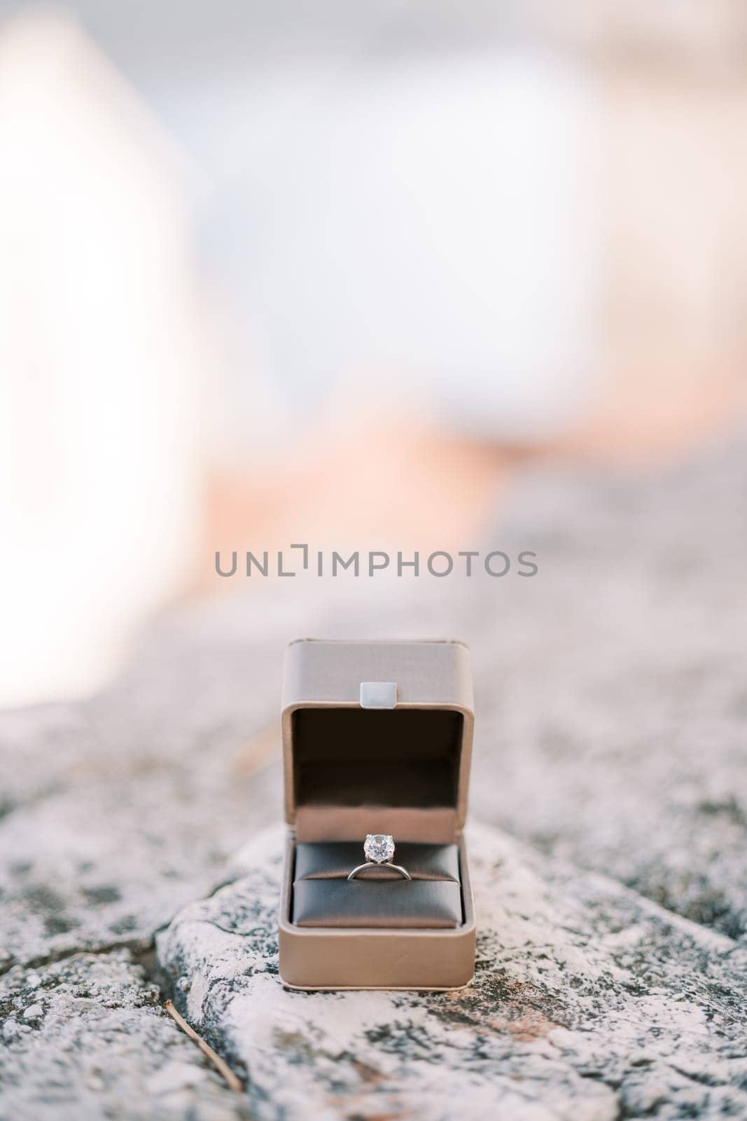 Engagement ring lies in an open box on a stone fence by Nadtochiy