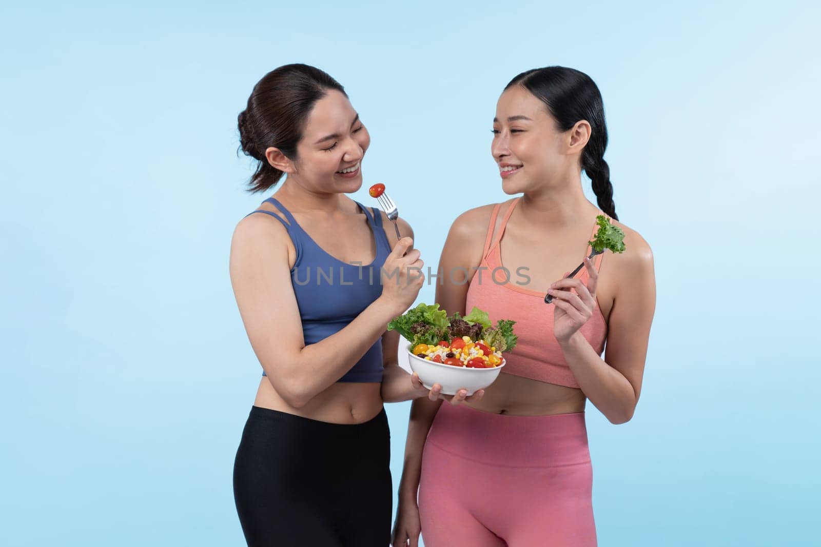 Two young sporty Asian women in sportswear holding salad bowl fill with fruit and vegetable. Natural youthful and fit body lifestyle people with balance nutrition on isolated background. Vigorous