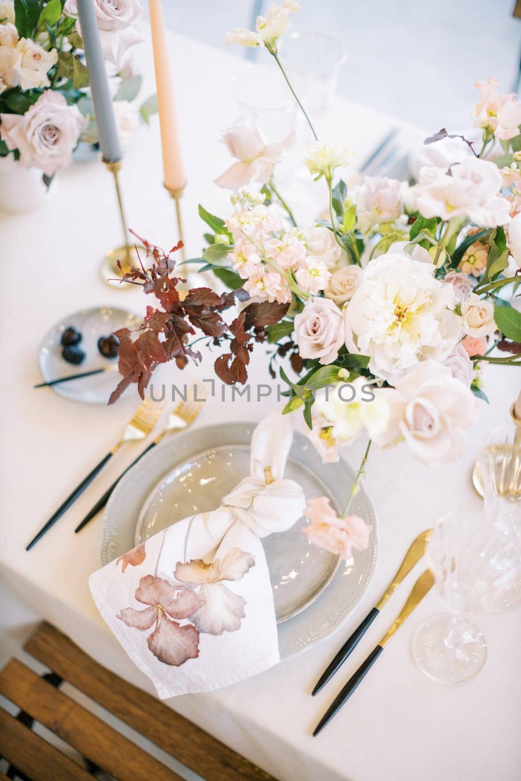 Knotted napkin lies on a plate near a bouquet of flowers on a set table. Top view by Nadtochiy