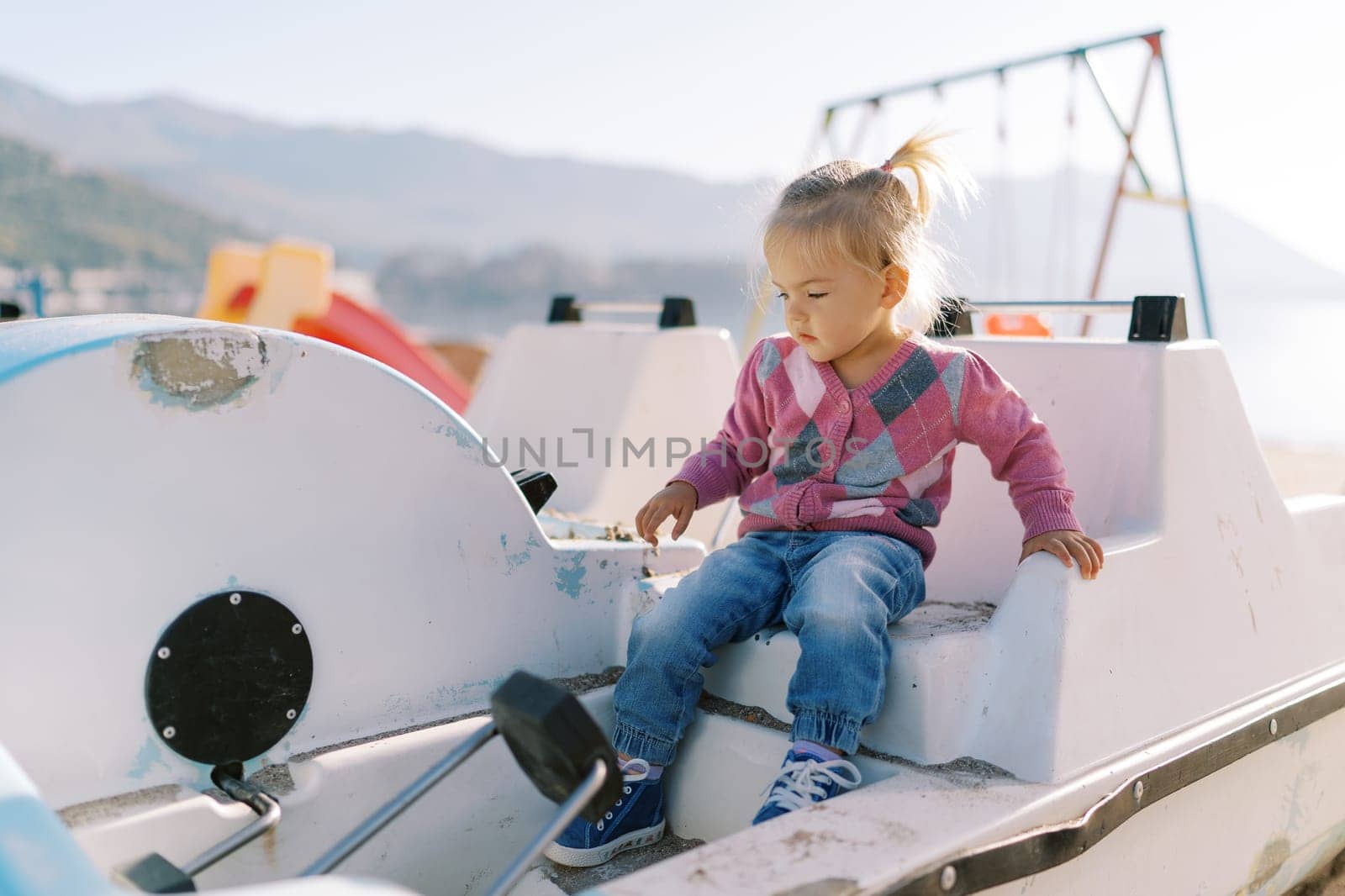 Little girl sits on the seat of a catamaran and looks at the pedals by Nadtochiy