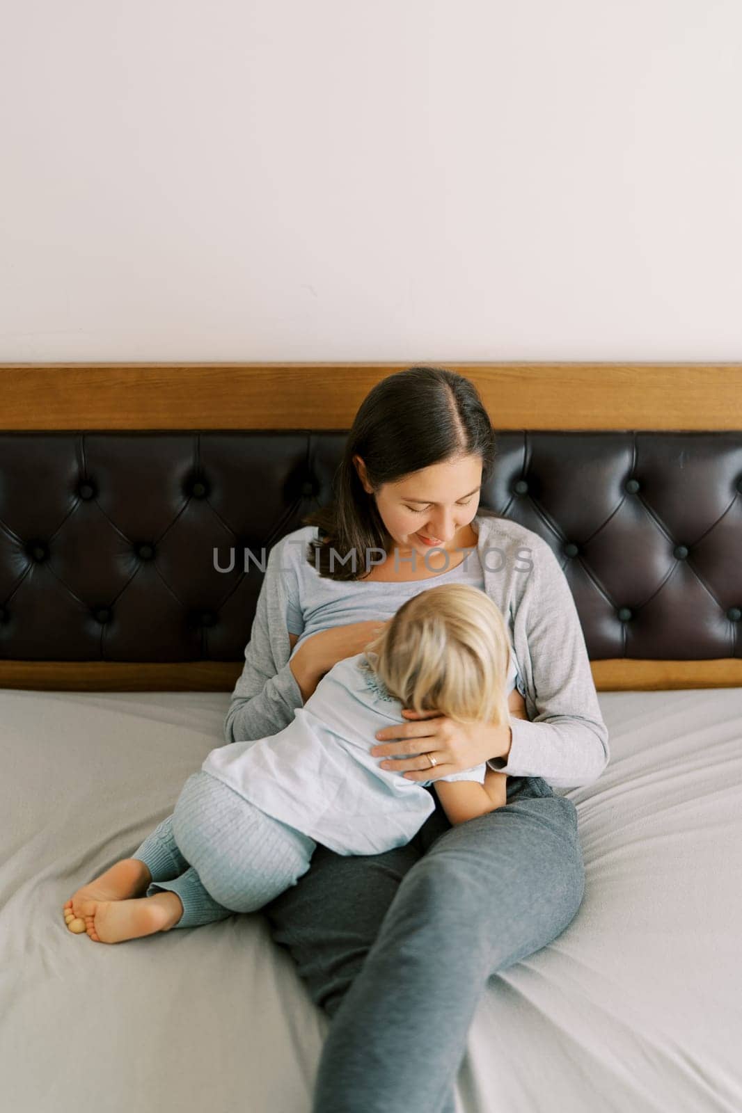 Mom breastfeeds a little girl, sitting on the bed. High quality photo