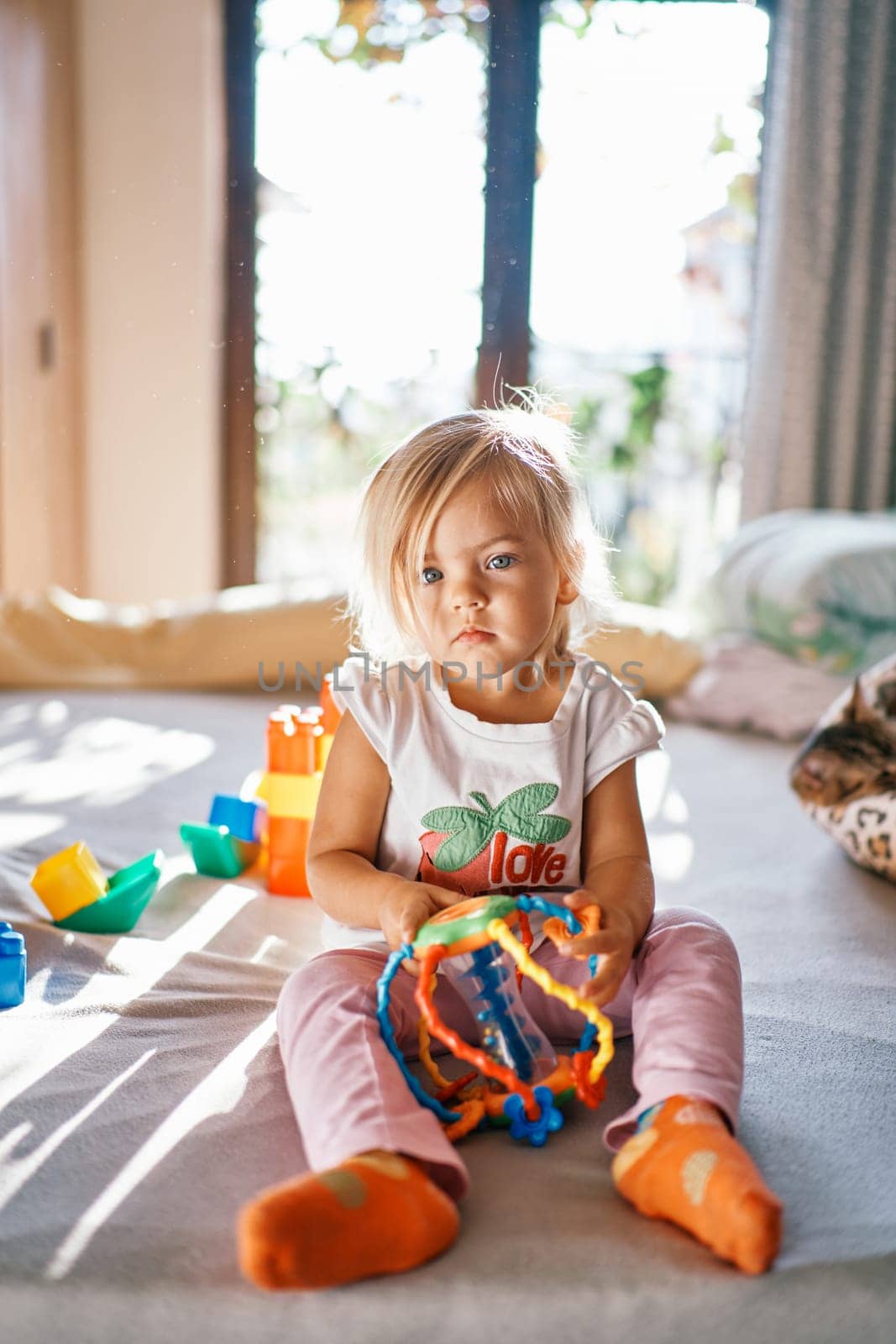 Little girl with puzzle rattle sits on the bed. High quality photo