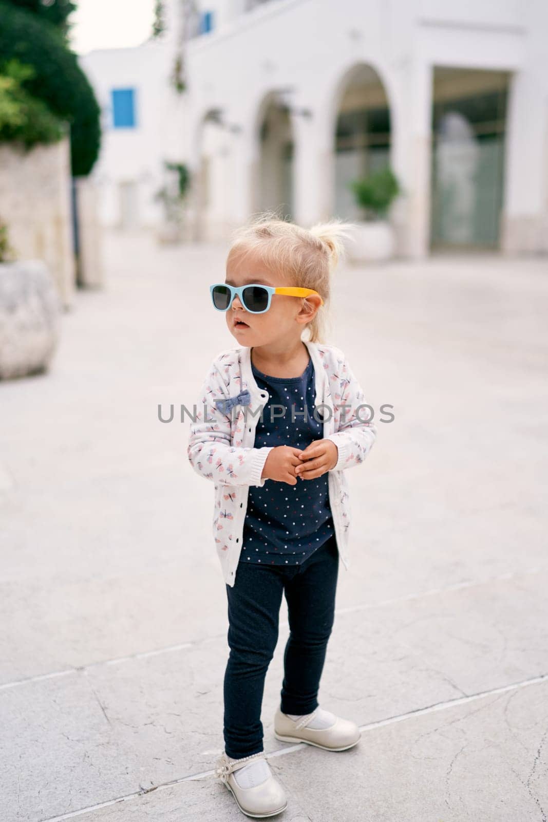 Little girl in sunglasses stands in the yard and looks away. High quality photo