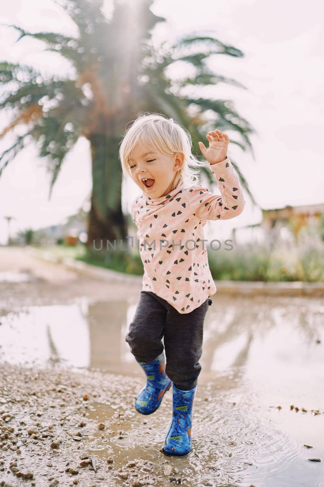 Smiling little girl in rubber boots jumping on a puddle. High quality photo