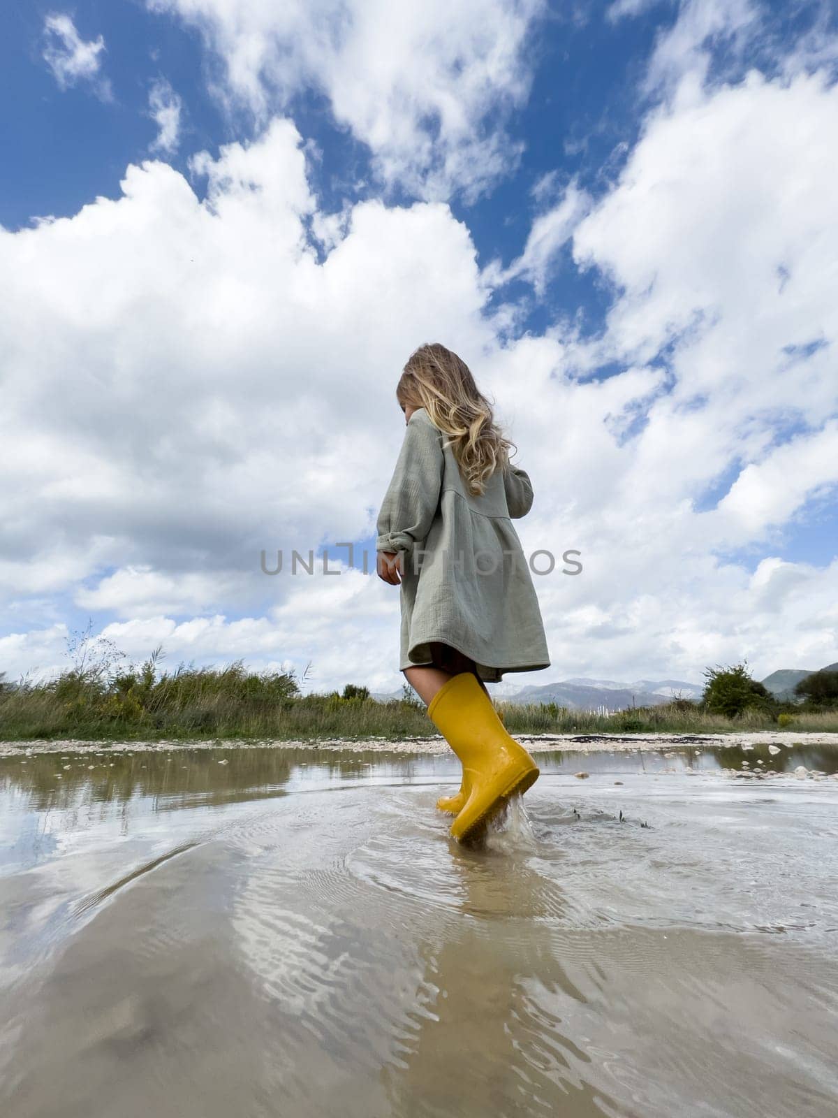 Little girl walks through a puddle raising splashes. High quality photo
