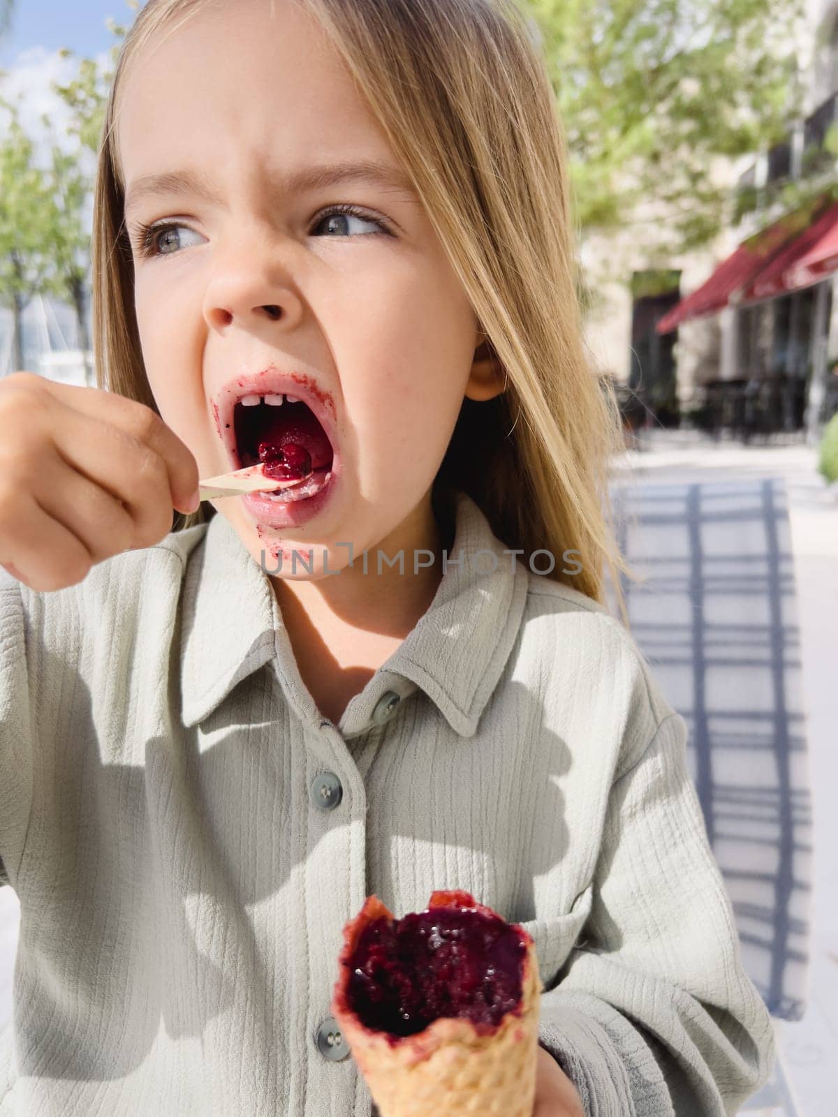 Little girl with stained mouth eating popsicles with a spoon. High quality photo