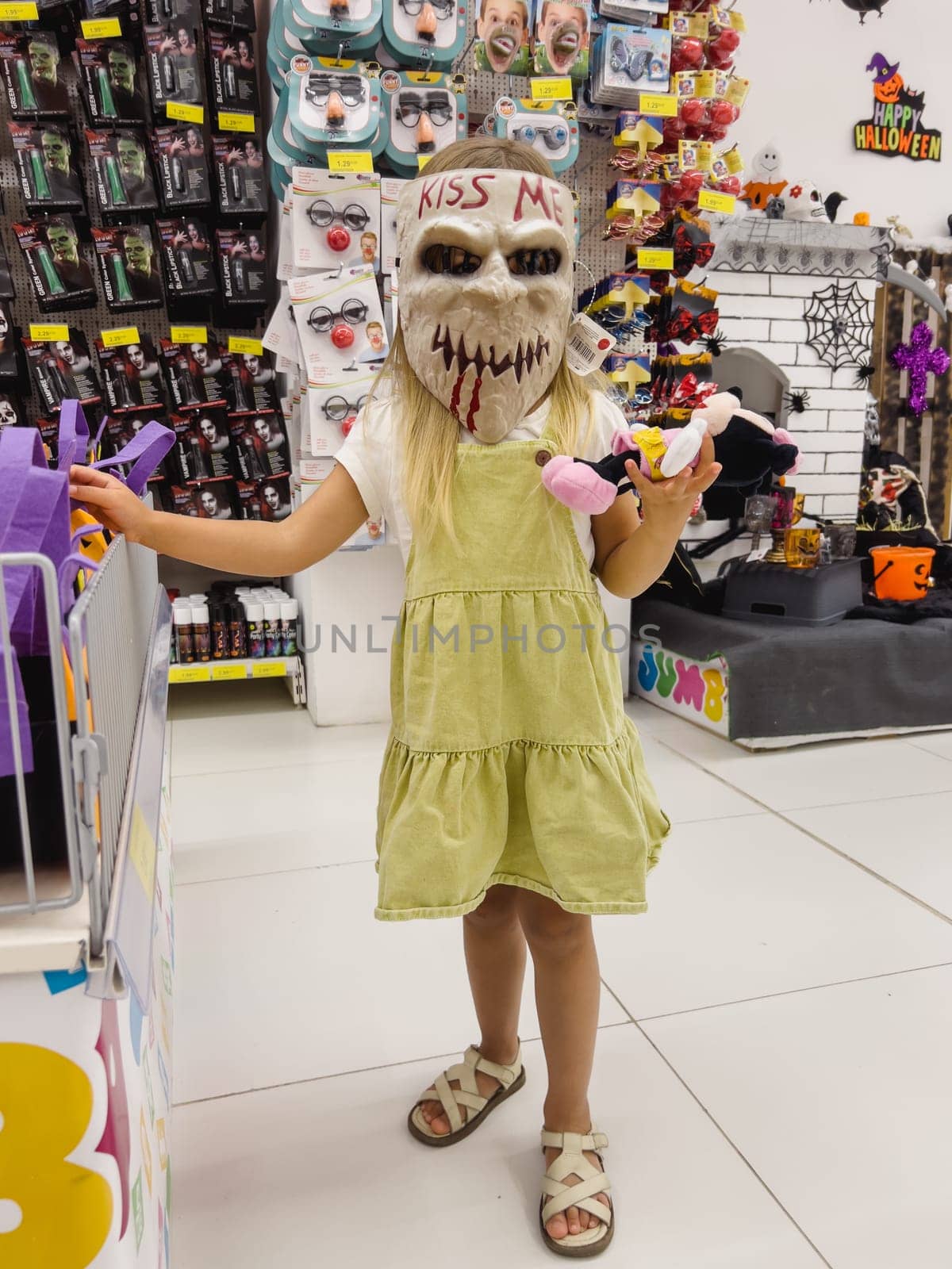 Little girl stands in a scary Halloween mask in a shop. High quality photo