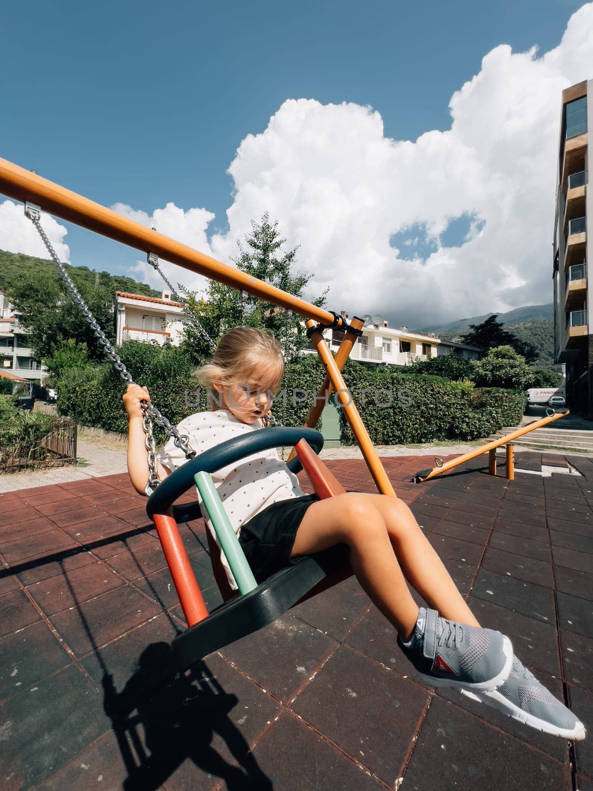 Little girl swings on a chain swing at the playground near the houses. High quality photo