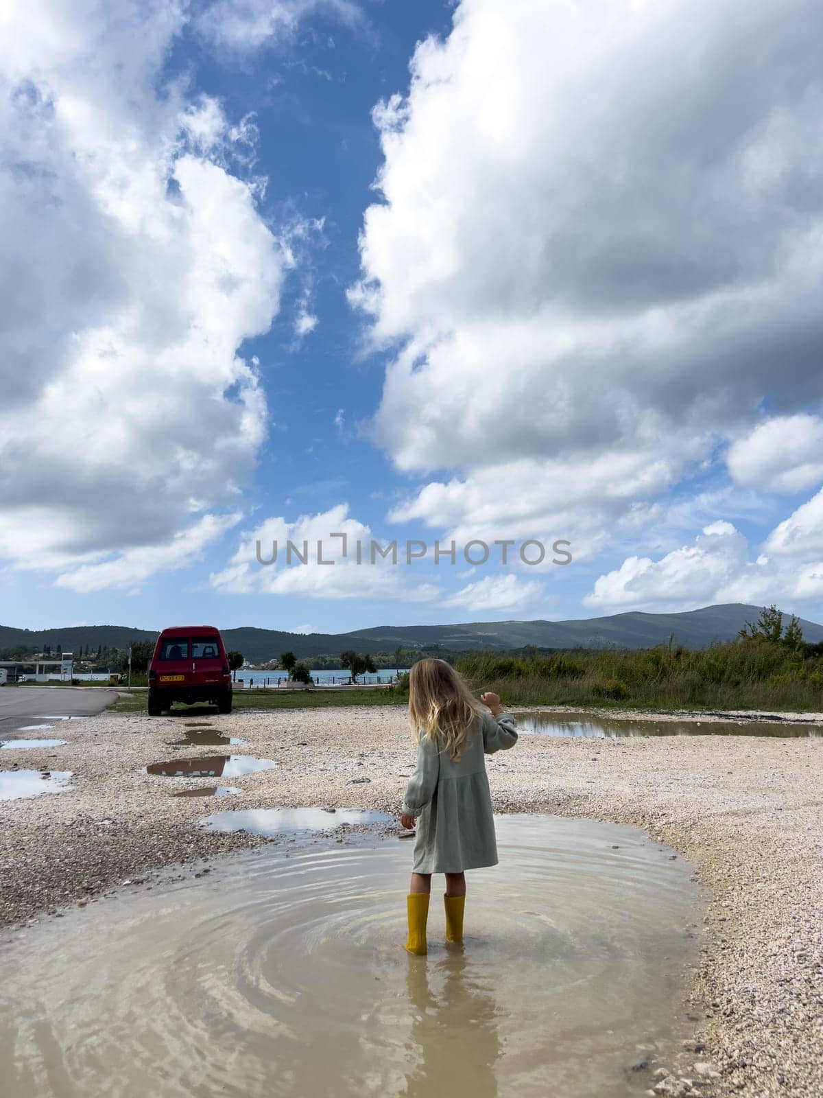 Little girl in rubber boots walks through a puddle and looks at the mountains. High quality photo