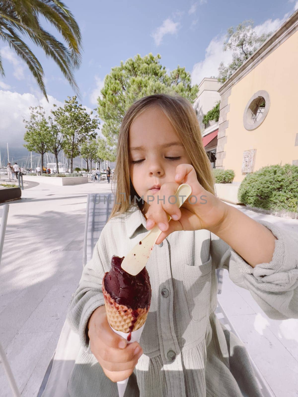 Little girl intently spooning popsicles from a waffle cone by Nadtochiy