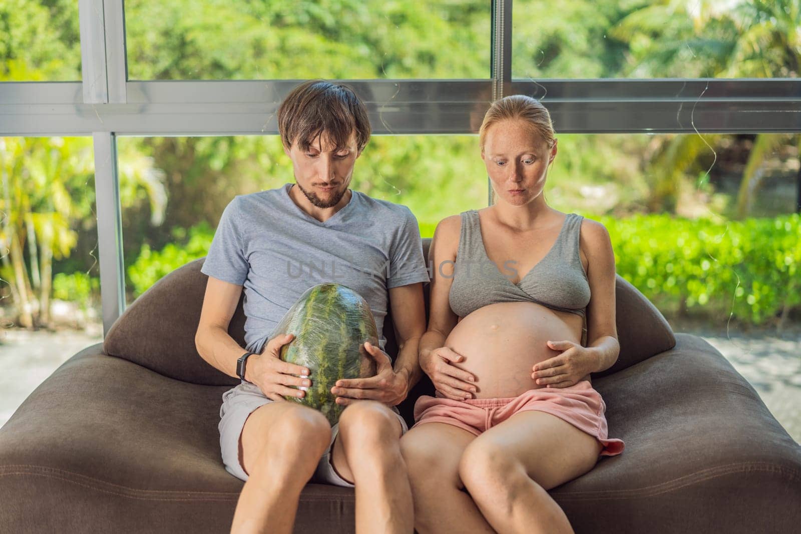 A humorous image: a pregnant woman and her husband playfully use a watermelon in place of a belly, comically highlighting the challenges of navigating with a pregnant bump.