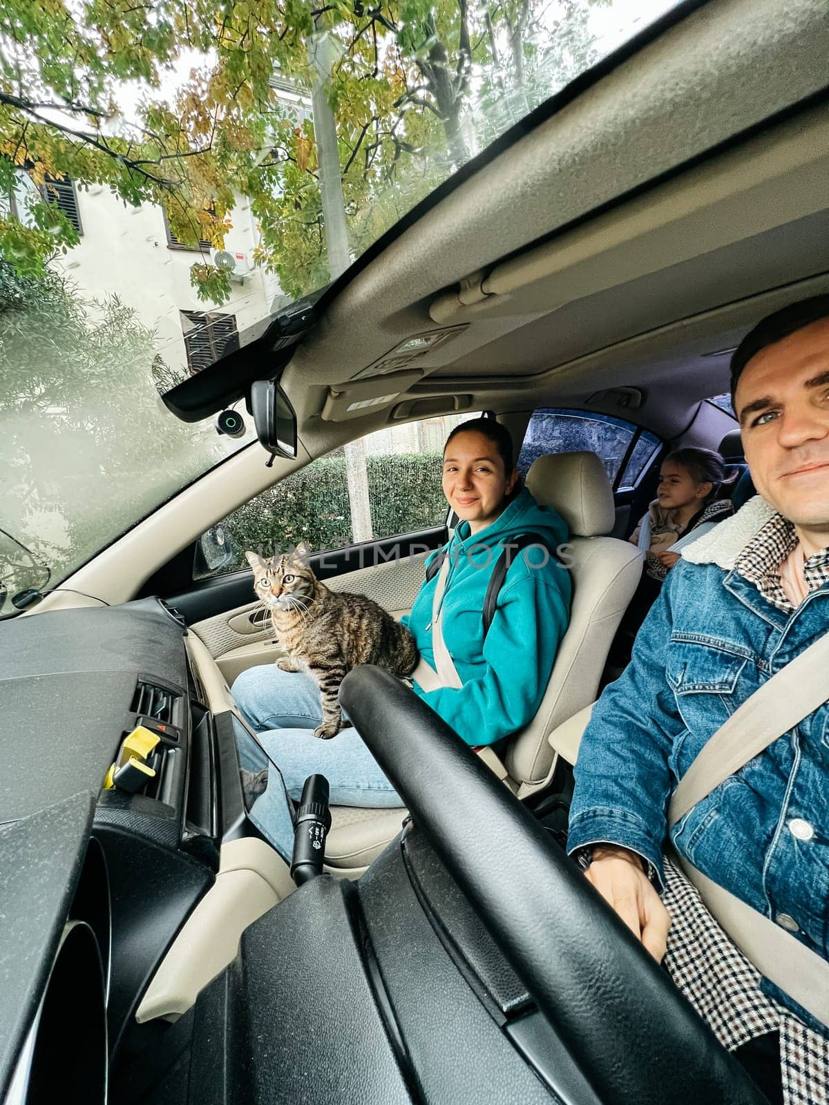 Mom, dad and a little girl are riding in a car with a cat by Nadtochiy