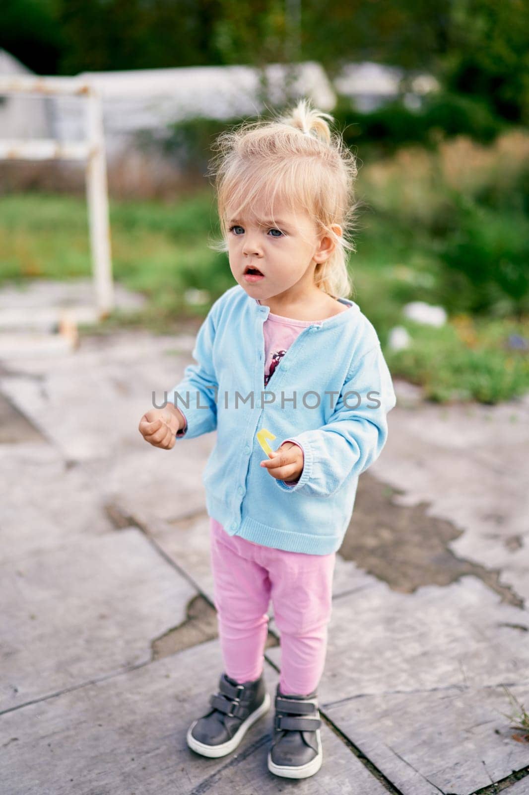 Little girl stands in the yard with her mouth open in surprise by Nadtochiy