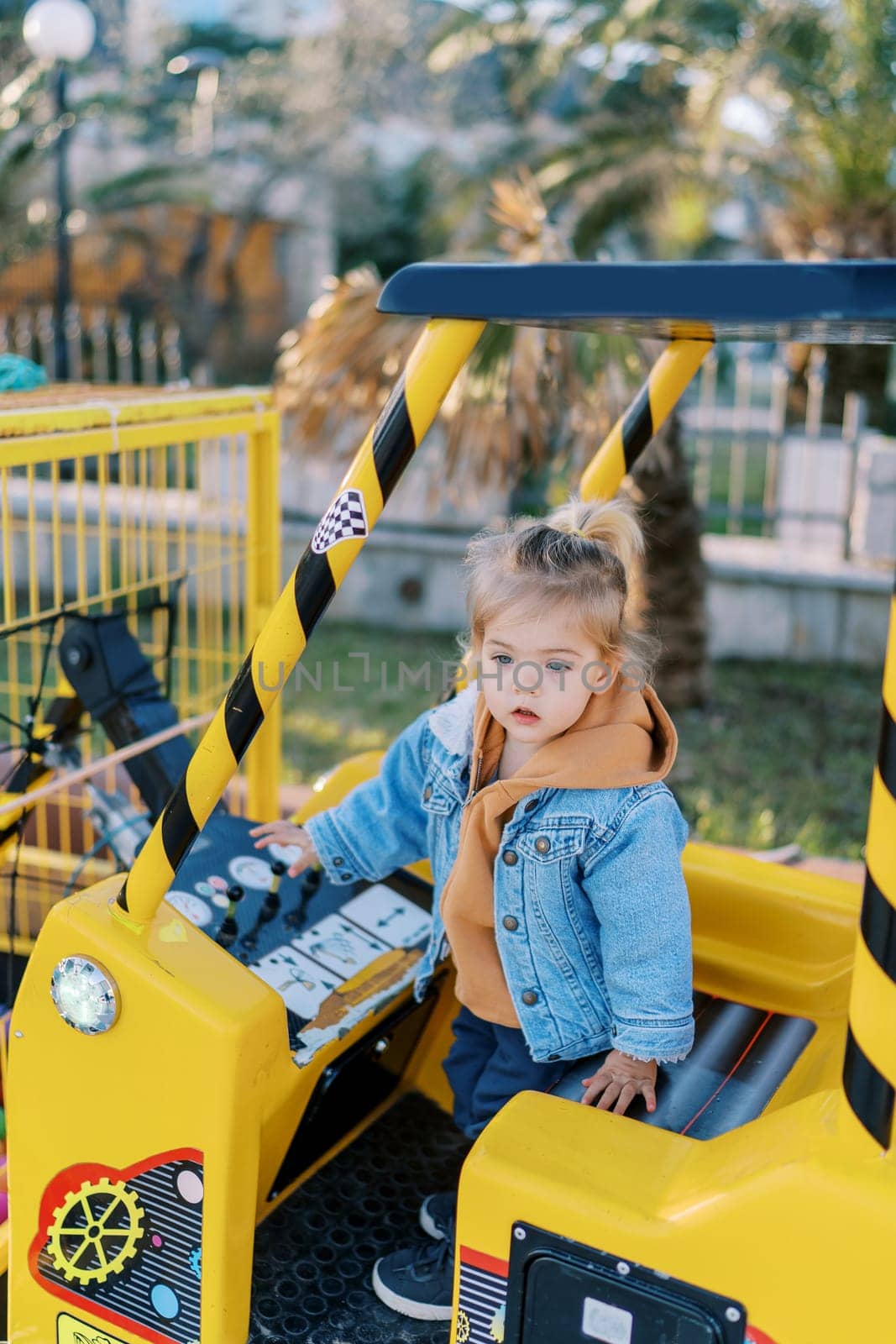 Little girl stands in the cab of a toy forklift and touches the levers of the control panel with her hand. High quality photo