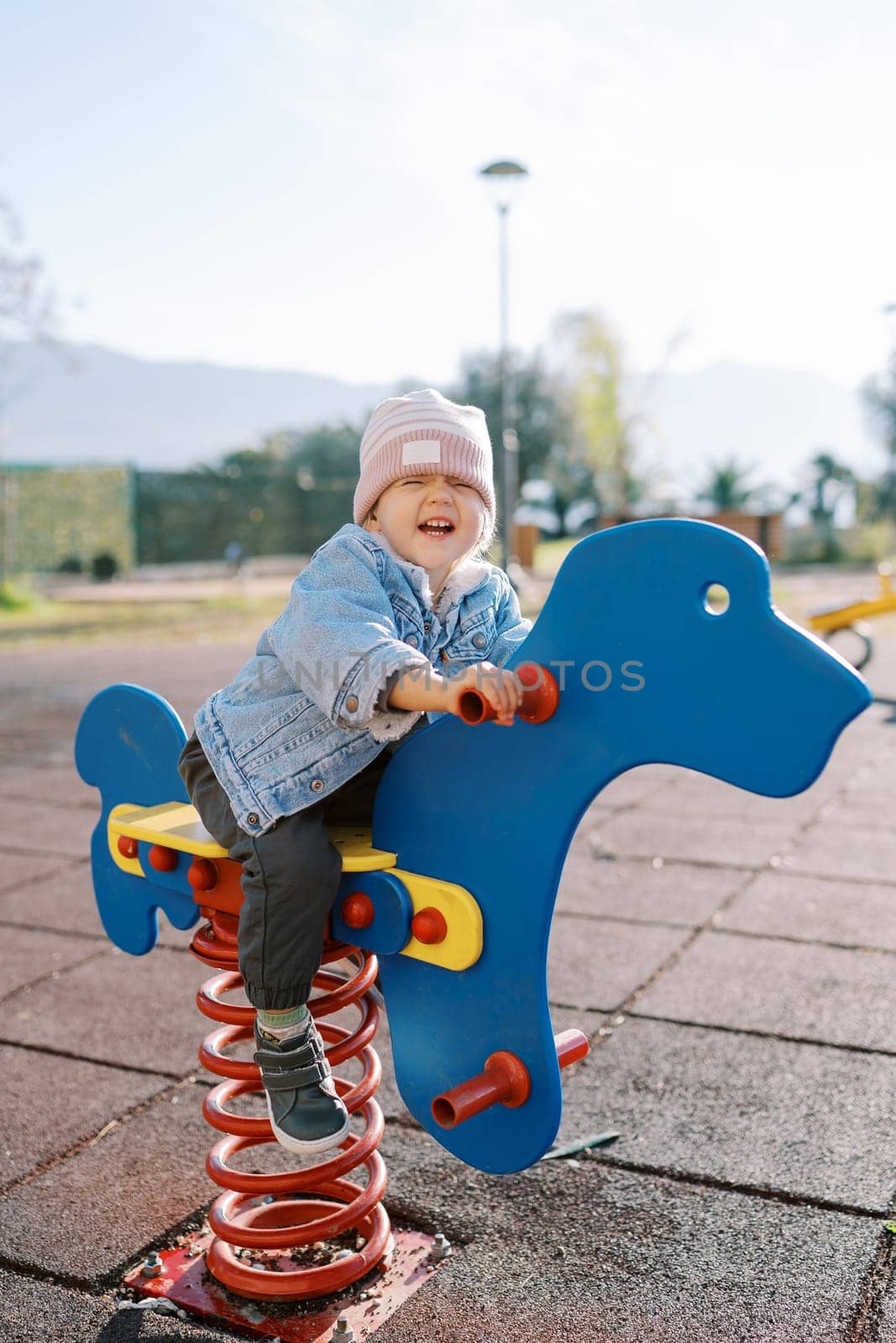 Little laughing girl swings on a swing-spring on the playground holding the handles. High quality photo